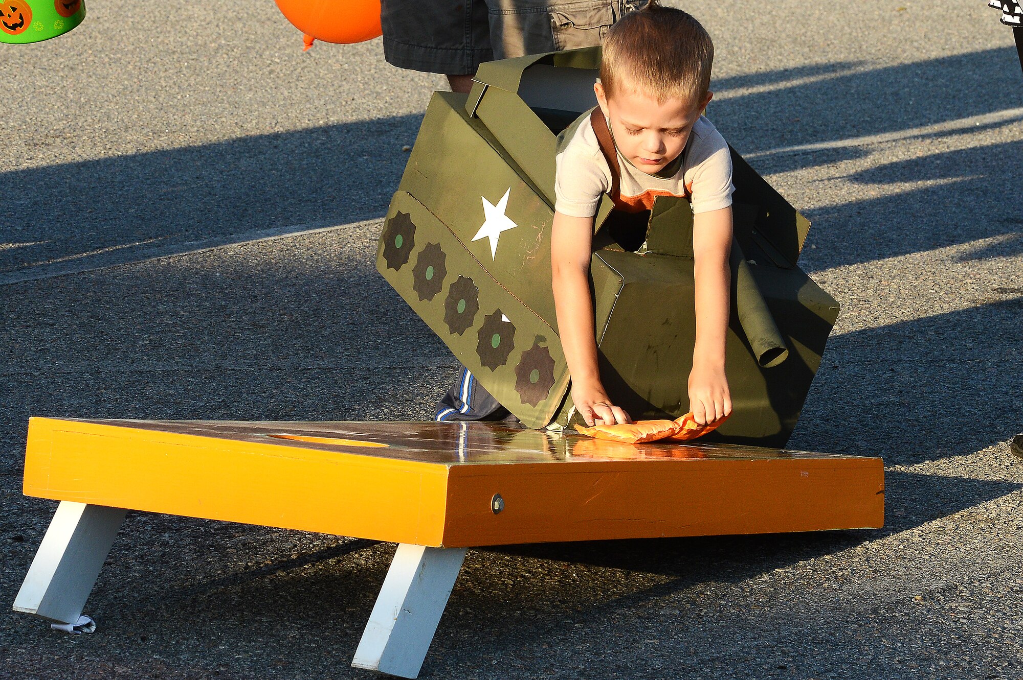 A Team Shaw child dressed as a tank picks up a bean bag before playing corn hole during Boo Bash at Shaw Air Force Base, S.C., Oct. 24, 2015. The Boo Bash featured a costume contest awarding prizes to the best costume in 10 categories, including best dressed family. (U.S. Air Force photo by Senior Airman Jonathan Bass/Released)