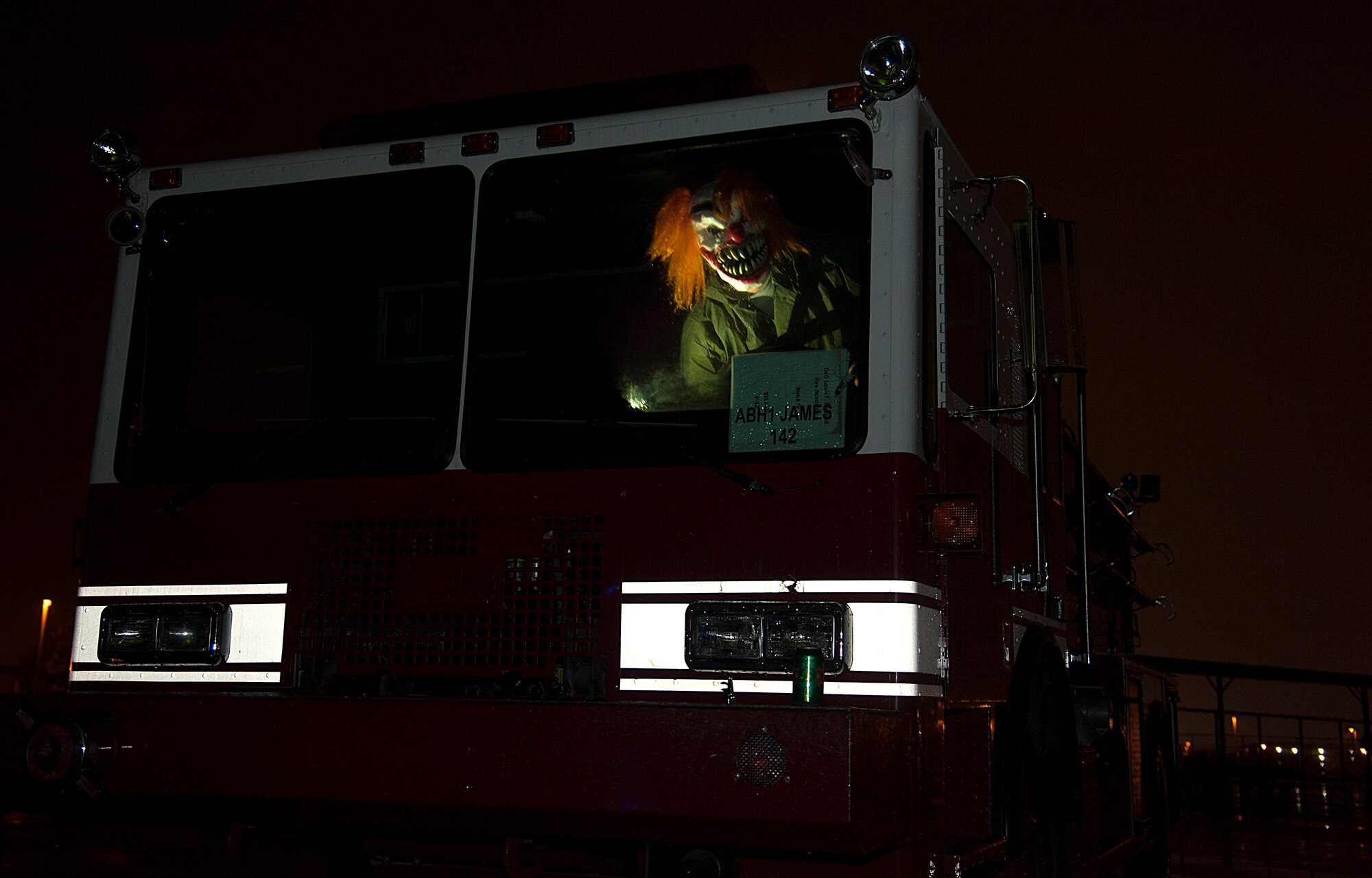 A volunteer dressed as a clown snickers behind the glass of a fire truck during the Ghoulfellow haunted house event at the Louis F. Garland Department of Defense Fire Academy training pad on Goodfellow Air Force Base, Texas, Oct. 24, 2015. Volunteers from various squadrons on base dressed up in costumes to play roles in the haunted house. (U.S. Air Force photo by Airman Caelynn Ferguson/Released)