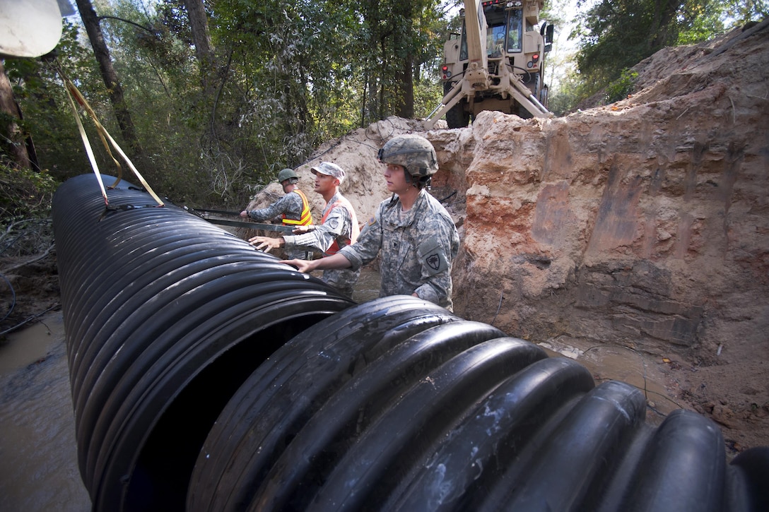 South Carolina Army National Guard Spc. Connor Ulyatt, right, and Sgt. Chase Gambill, center, align a section of culvert pipe as engineers work to replace a washed out culvert in Gilbert, S.C., Oct. 24, 2015. Ulyatt is assigned to the 1221st Engineering Company and Gambill is assigned to the 124th Engineering Company. South Carolina Army National Guard photo by Sgt. Brian Calhoun