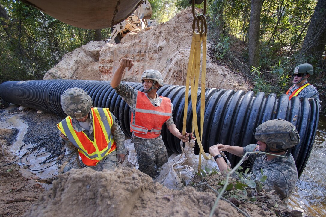 South Carolina Army National Guard Sgt. Chase Gambill, center, directs the hydraulic excavator operator while placing sand bags to replace a washed out culvert on a Lexington County road in Gilbert, S.C., Oct. 24, 2015. Gambill is assigned to the 124th Engineering Company. South Carolina Army National Guard photo by Sgt. Brian Calhoun