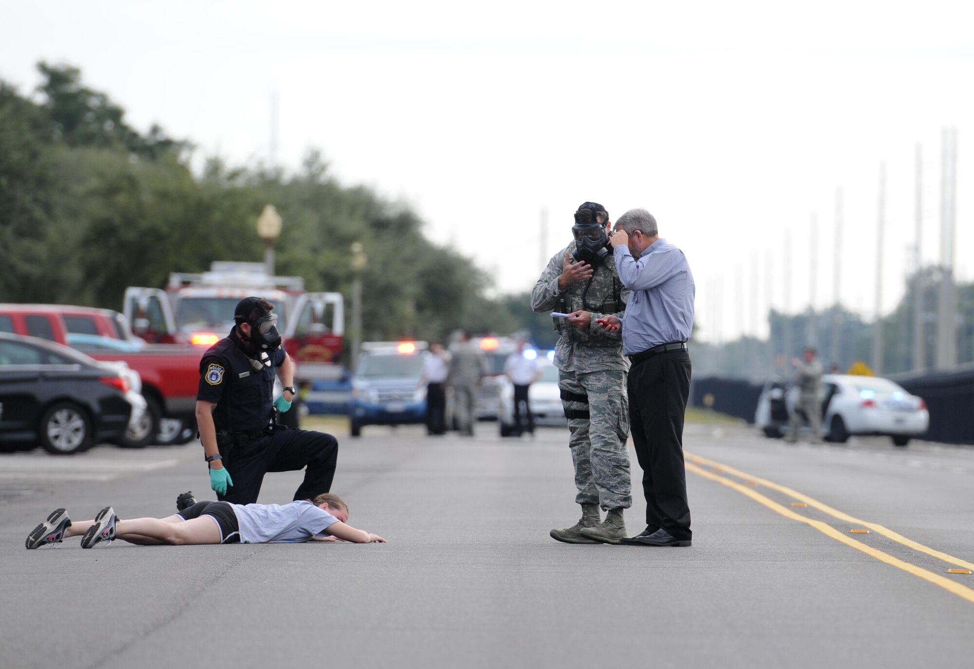 Senior Airman Mikayla Dunne, 81st Dental Squadron dental technician, lays on the ground as a “victim” as an inspection team and first responders discuss the scenario during a Chemical, Biological, Radiological and Nuclear exercise scenario, Oct. 22, 2015, Keesler Air Force Base, Miss. The Force Protection Condition exercise scenario included an intruder simulating releasing gas to cause a mass casualty event. Airmen who were returning from physical training simulated receiving skin, eye and lung burns from exposure to the chemical. (U.S. Air Force photo by Kemberly Groue)