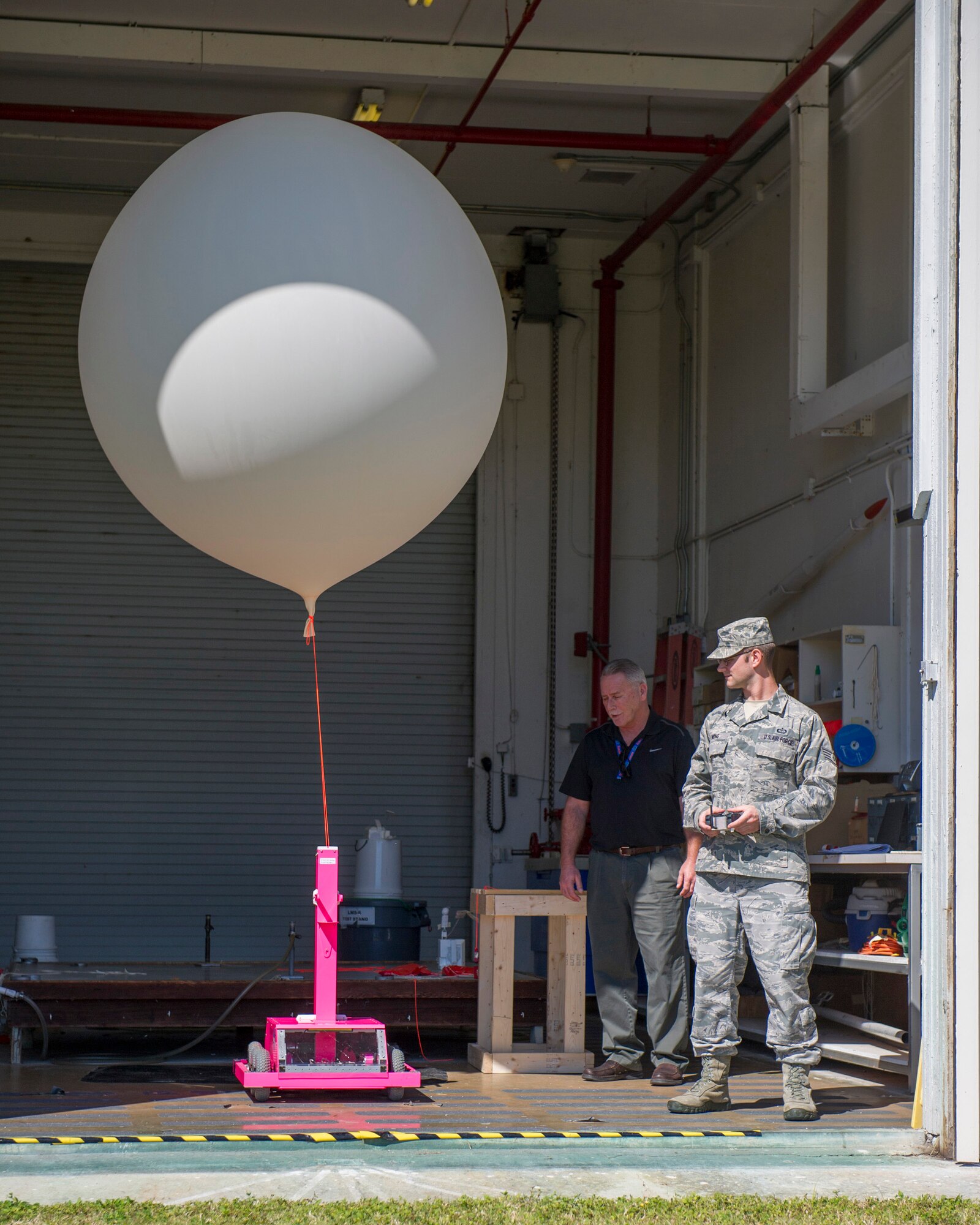 Thomas Taylor, 45th Weather Squadron chief of standardization and evaluation, and Staff Sgt. Matthew Mong, 45th WS NCO in charge training, demonstrates how to use, Pink, a Weather-Bot robot used to help members of the 45th WS release weather balloons without risking human life during lighting, Jan. 27, 2015, at Cape Canaveral Air Force Station, Fla. Many Brevard County students teamed-up with CCAFS and NASA to help better determine weather conditions during rocket launches.  (U.S. Air Force photo/Matthew Jurgens) (Released)  