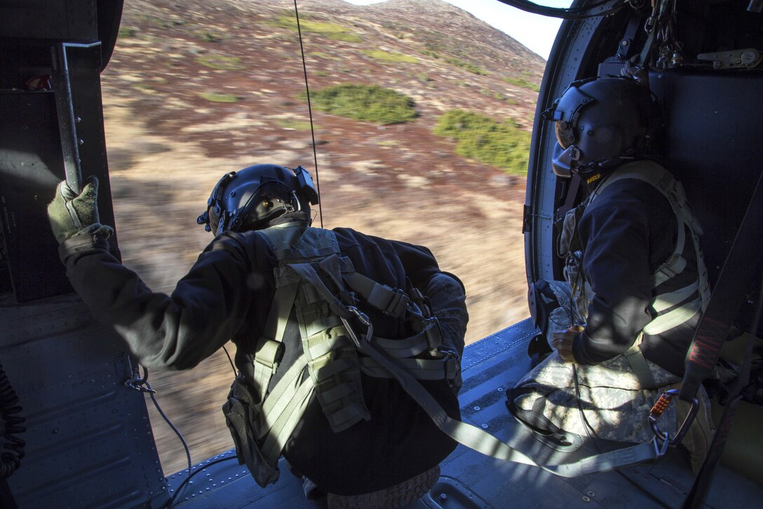 Army Sgt. Bradley McKenzie, left, and Staff Sgt. Kevan Katkus look out the side of their UH-60 Black Hawk helicopter for safety clearance while conducting flight operations over Joint Base Elmendorf-Richardson, Alaska, Oct. 21, 2015. McKenzie and Katkus are crew chiefs assigned to the Alaska Army National Guard's 1st Battalion, 207th Aviation Regiment. U.S. Air Force photo by Alejandro Pena