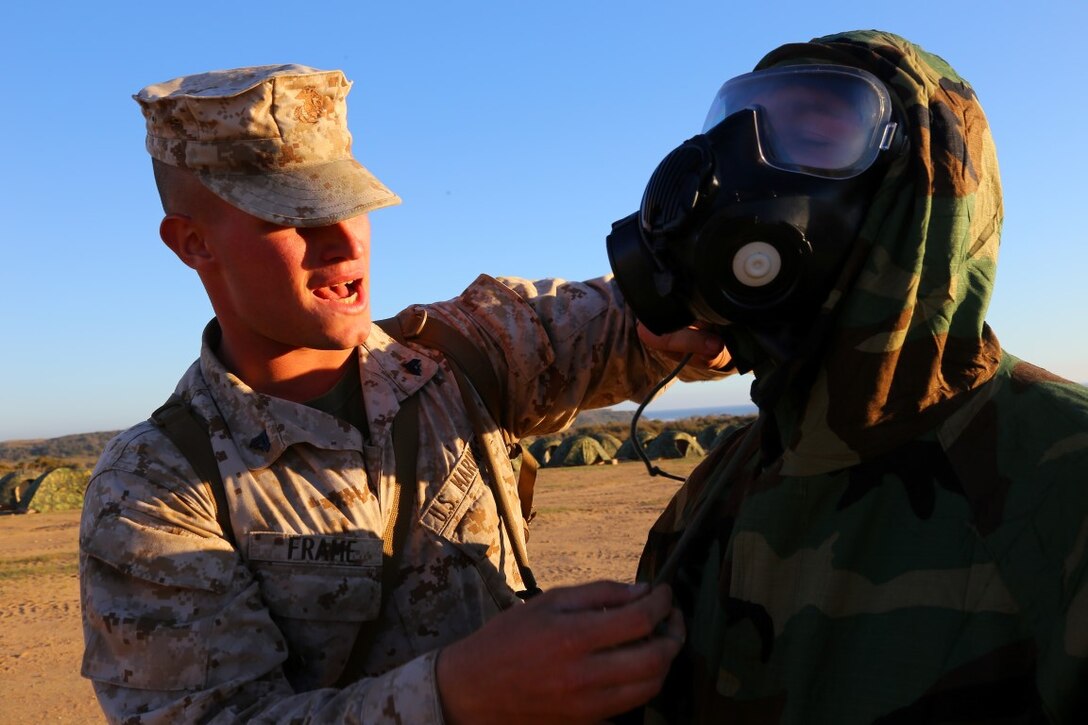 Cpl. Matthew J. Frame, left, a chemical, biological, radioactive, and nuclear (CBRN) defense specialist with the 11th Marine Expeditionary Unit (11th MEU), demonstrates the proper technique of putting on the mission oriented protective posture (MOPP) coate as part of CBRN training during the 11th MEU command element field exercise (CEFEX). CBRN training teaches Marines how to utilize their issued MOPP gear enabling them to survive in a CBRN environment. (U.S. Marine Corps photo by Gunnery Sgt. Rome M. Lazarus/Released)
