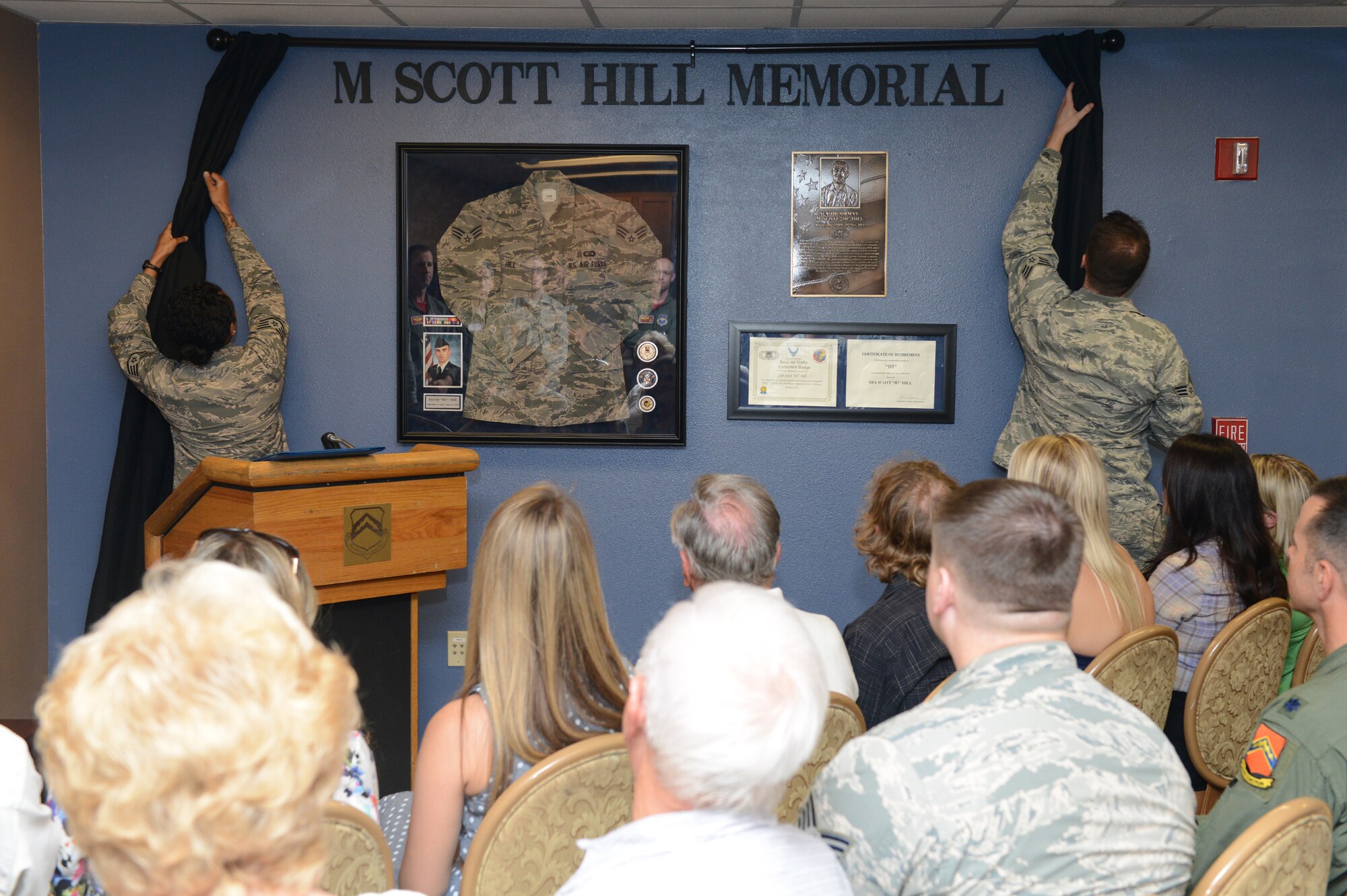 Staff Sgt. Alexena Simien, 56th Operations Support Squadron air traffic controller, and Senior Airman Samuel Bricker, 56th OSS air traffic controller, unveil Senior Airman Scott Hill’s memorial wall during a dedication ceremony at Luke Air Force Base, Arizona, Oct. 26, 2015. Hill lost his battle with cancer and passed away May 18, 2014. The ceremony also retired Hill’s air traffic controller initials: HI. The initials are a special identifier for controllers and HI will be Hill’s at Luke forever. (U.S. Air Force photo by Senior Airman James Hensley)