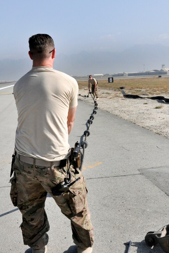 U.S. Air Force Staff Sgt. Timothy Shearer and Senior Airman Yves Meillarec work on the aircraft arresting cable system on Bagram Airfield, Afghanistan, Oct. 22, 2015. Shearer and Meillarec are assigned to the 455th Expeditionary Civil Engineer Squadron. Pilots will engage the arresting system during some precautionary landings to help slow or stop their aircraft.