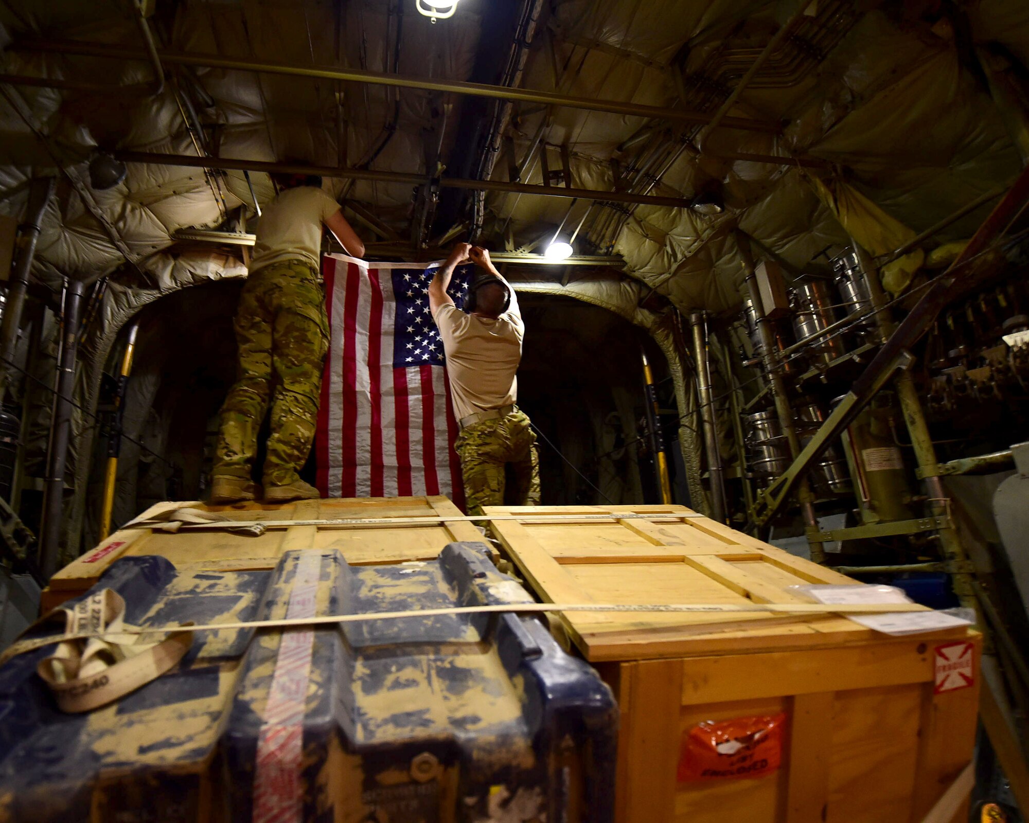 Senior Airman Erin Stewart, right, and Chief Master Sgt. Thomas Glover, 737th Expeditionary Airlift Squadron loadmasters, hang a U.S. flag onboard a C-130H Hercules during an airlift mission in Southwest Asia, Oct. 27, 2015. Stewart and Glover are two of nearly one hundred members deployed from the 192nd Airlift Squadron based out of Reno, Nevada. Their team has flown more than 600 missions during their deployment. (U.S. Air Force photo by Staff Sgt. Jerilyn Quintanilla)