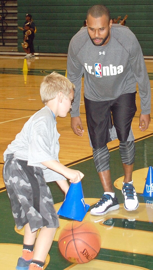 Spurs guard Patty Mills helps a Jr. NBA clinic participant work on his dribbling skills at Cole High School on Joint Base San Antonio-Fort Sam Houston Oct. 19. Seventy-five military children participated in the clinic, the tip off of the NBA’s Jr. NBA Week.
