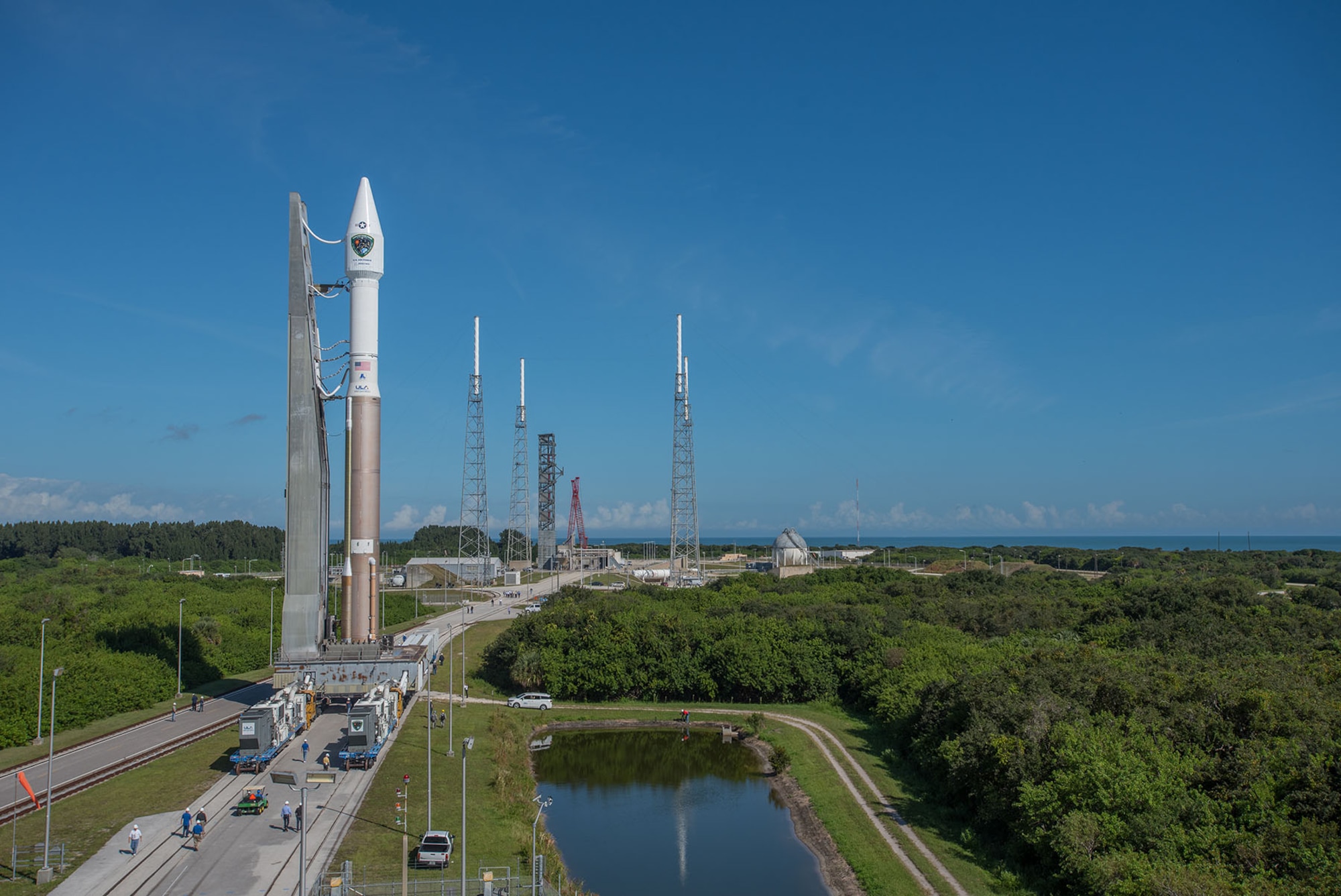 A wide angle view of the Atlas V 401 launch vehicle with GPS IIF-11 satellite aboard is rolled from the Vertical Integration Facility to Space Launch Complex-41 in anticipation of a Saturday afternoon launch from Cape Canaveral Air Force Station, Fla. The launch window opens Oct. 31 at 12:13 EDT (9:13 a.m. PDT). This is the second to last GPS IIF launch in a series of 12 spacecraft. The gray structure in the distance just to the left of the red construction crane is a new Crew Access Tower, currently nearing completion for future use by astronauts with the Boeing CST-100 manned spacecraft, slated for first flight in December 2017. (Photo courtesy United Launch Alliance).