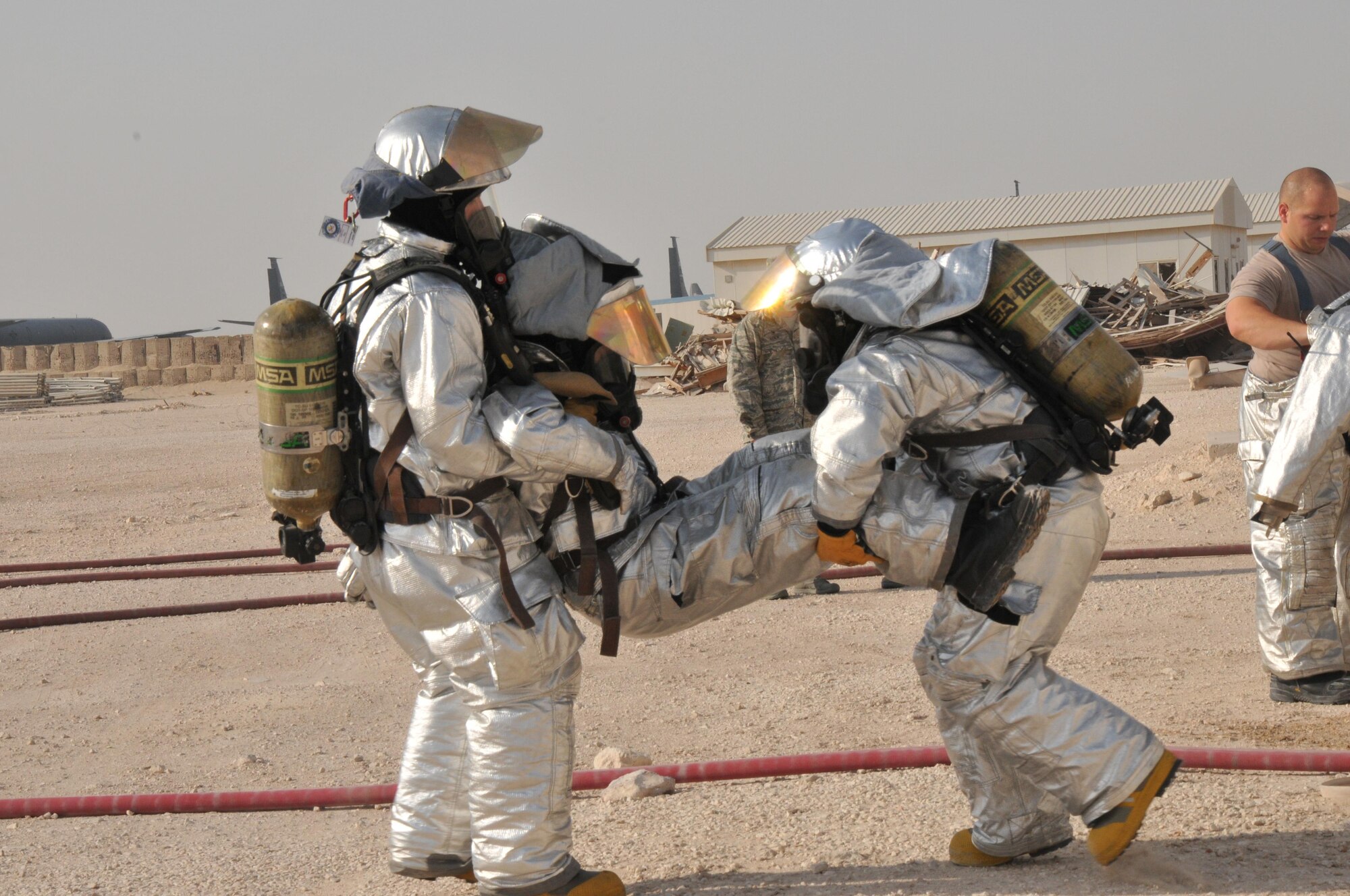 Two 379th Expeditionary Civil Engineer Squadron firefighters carry one of their fellow firefighters out of a simulated burning building during an interagency exercise in Al Udeid Air Base, Qatar Oct. 27. The injured firefighter stepped on a mock explosive device which required him to be rescued from the building. The interagency exercise featured professionals from three 379th Air Expeditionary Wing units including explosive ordnance technicians, security forces patrolmen and firefighters. (U.S. Air Force photo by Tech. Sgt. Terrica Y. Jones/Released)