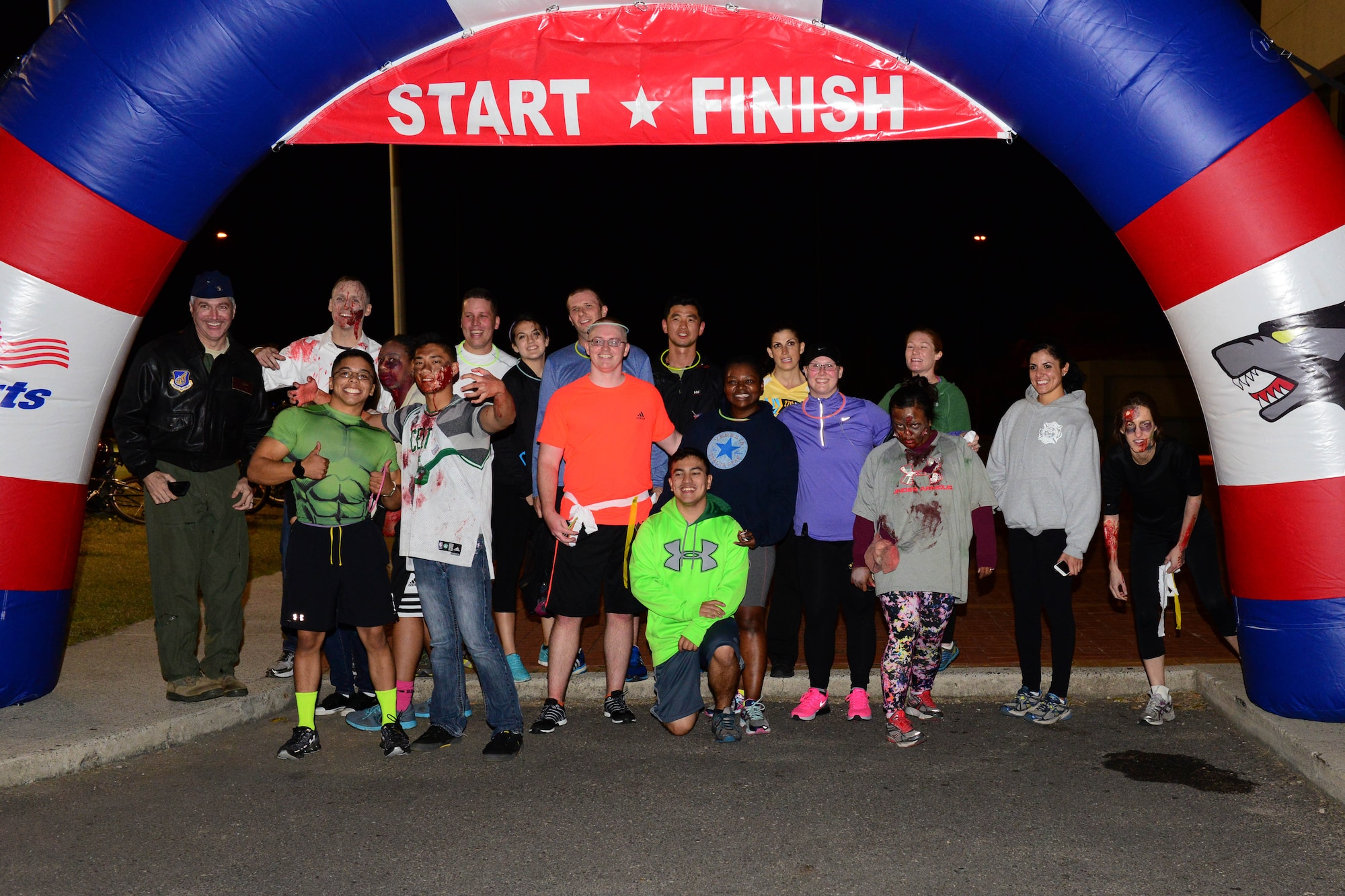 Col. Jeremy T. Sloane, 8th Fighter Wing commander, and Col. Juris Jansons, 8th FW vice commander (left to right) takes a photo at the finish line with the participants of the zombie run held at Kunsan Air Base, Republic of Korea, Oct. 28, 2015. The zombies spooked 16 runners for 3.7 kilometers as they made their way around a portion of the base. (U.S. Air Force photo by Senior Airman Ashley L. Gardner/Released)