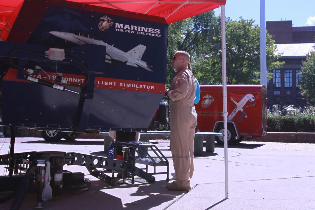 U.S. Marine Corps Capt. Richard Jacobs, the 4th Marine Corps District aviation assistant for officer procurement and Millville, Pa., native, assists a University of Michigan student in flying an F-18 Hornet simulator Sept. 21, 2015. The Marines bring the simulators to college campuses to build awareness and enthusiasm among the students and campus faculty regarding Marine aviation programs. (U.S. Marine Corps photo by Sgt. J. R. Heins/ Released)