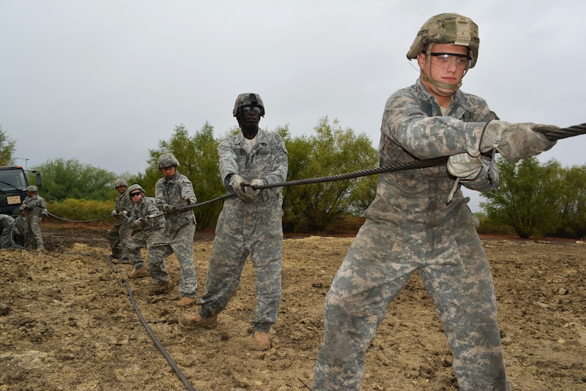 Students attending the Wheeled Vehicle Recovery Course at Regional Training Site Maintenance-Fort Hood, Texas, unravel a winch cable from a tow truck to connect the cable to a truck wedged in mud, Oct. 23, 2015. The course teaches Army mechanics how to properly and safely recover and tow vehicles that may be stuck or inoperable.