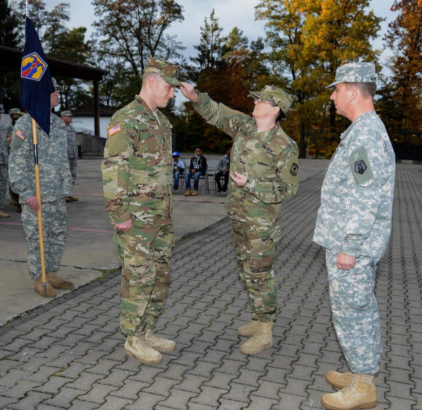 Army Reserve Staff Sgt. Linda Maybury (center) places a hat on her son, newly promoted Army Reserve Sgt. 1st Class David Maybury, during his promotion ceremony Oct. 25, 2015 at Panzer Kaserne in Kaiserslautern, Germany.  Maj. Paul Nuernberg, 7th Mission Support Command Headquarters, Headquarters Company, presides. David is an active Guard Reserve Soldier assigned to the 7th MSC's HHC. Linda is also an AGR Soldier assigned to the 361st Civil Affairs Brigade. (U.S. Army photo by Visual Information Specialist Elisabeth Paque/Released)