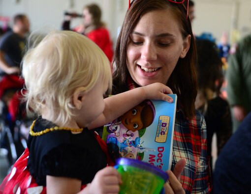 Rachel Clausen gives her daughter Francesca, one, a free book from the Blue Star Military group during the 2015 children's halloween party Oct. 30, 2015, at Creech Air Force Base, Nevada. Activities for the day included cornhole, trunk or treat, book reading, free food, bag decoration, and a magic show. (U.S. Air Force photo by Airman 1st Class Christian Clausen/Released)
