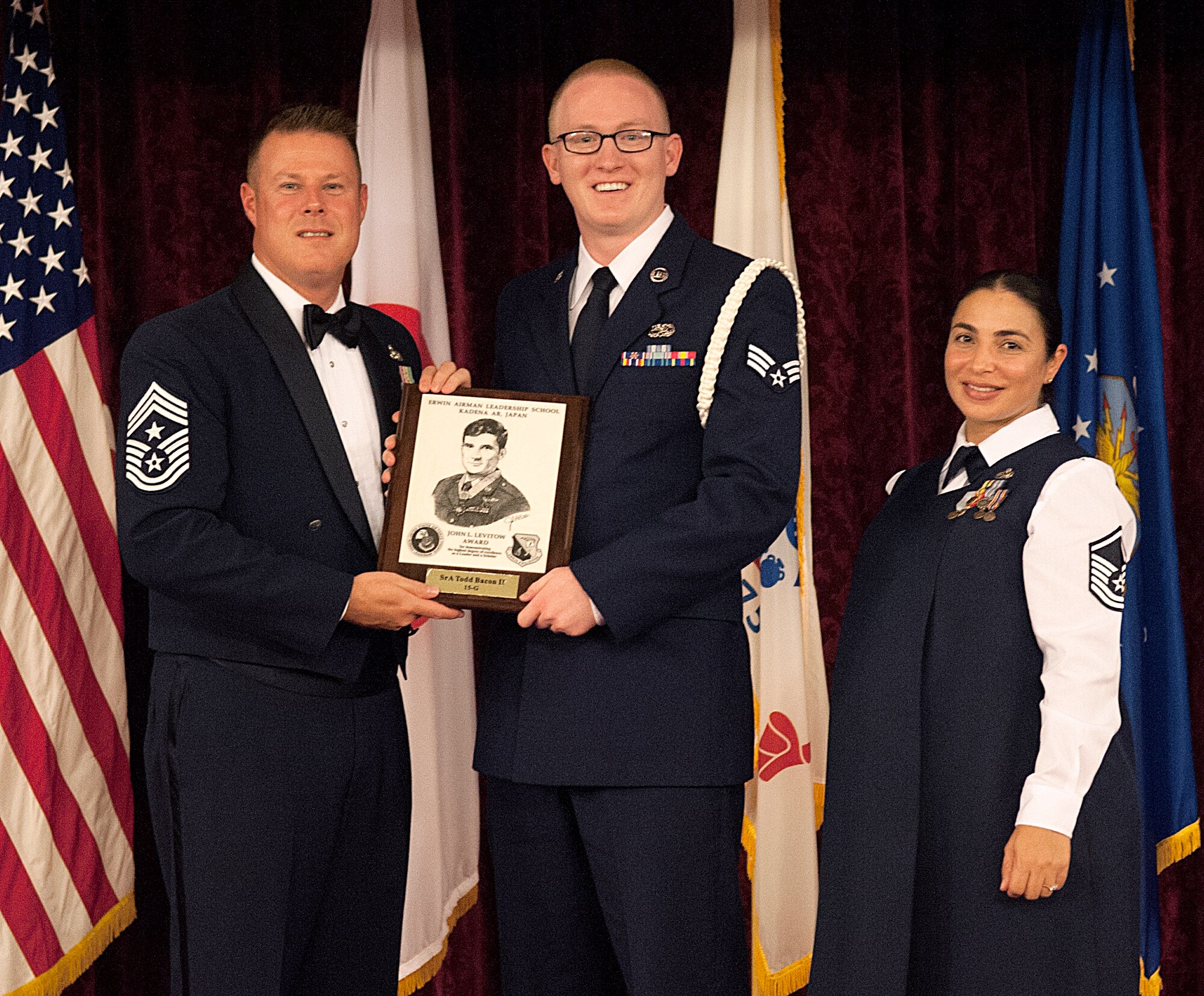 U.S. Air Force Senior Airman Todd Bacon, 718th Aircraft Maintenance Squadron composite tool kit custodian, receives the John L. Levitow Award from Chief Master Sgt. Charles Hoffman, 18th Wing command chief, with Master Sgt. Edith Smith, 353rd Special Operations Maintenance Squadron Maintenance Operations Flight chief, during the graduation ceremony for ALS Class 15-G on Kadena Air Base, Japan, Oct. 26, 2015. The John L. Levitow Award is presented to the Airman who most demonstrates outstanding leadership and scholastic achievement during Airmen Leadership School. (U.S. Air Force photo by Airman 1st Class Nicholas Emerick)