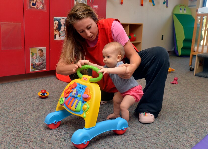 Zelia Mersinger, 56th Force Support Squadron child development center educational technician, helps a baby onto her walker at the Child Development Center at Luke Air Force Base, Ariz., Oct. 7, 2015. The CDC accepts children with reservations and a space-available, drop-in basis. A child may stay for a few hours or spend the entire day on a limited basis. The center also has an active sublet program for parents seeking temporary care. (U.S. Air Force photo by Senior Airman Devante Williams)