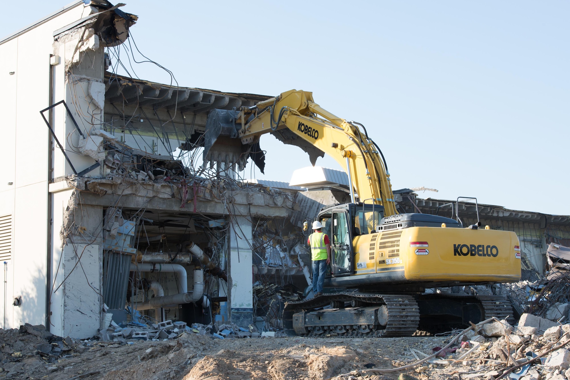 Col. Michele Edmondson, 81st Training Wing commander, receives instructions from Jamie Bean, base operations support contractor, as she operates an excavator to continue the demolition of Hewes Hall, August 28, 2015, at Keesler Air Force Base, Miss. In addition to helping the Air Force plan to reduce its footprint by 20% before 2020, the building was also demolished because it was within the clear zone of the air field. (U.S. Air Force photo by Marie Floyd)