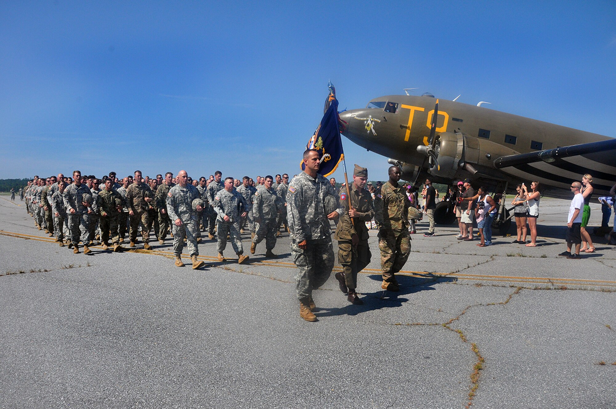 Led by Lt. Col. Korey Brown, paratroopers taking part in the airborne anniversary celebrations march from the drop zone past a vintage C-47 Skytrain as visitors look on. (Photo by Gene H. Hughes)
