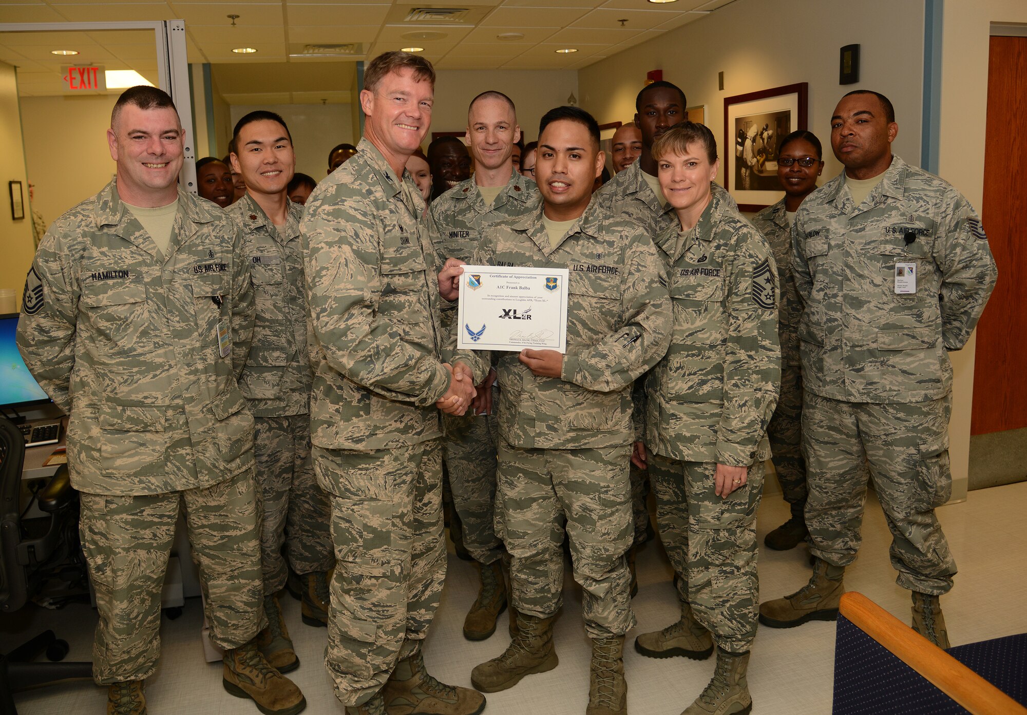 Airman 1st Class Frank Balba, center, 47th Medical Operations Squadron bioenvironmental engineering technician, poses with Col. Thomas Shank, 47th Flying Training Wing commander, and Chief Master Sgt. Teresa Clapper, 47th FTW command chief, after accepting the “XLer of the Week” award, here, Sep. 2, 2015. The “XLer” is a weekly award chosen by wing leadership and is presented to those who consistently make outstanding contributions to their unit and Laughlin. (U.S. Air Force photo by Airman 1st Class Ariel D. Partlow)