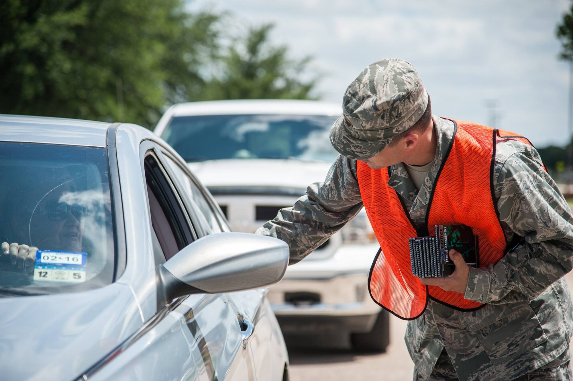 U.S. Air Force Maj. David A. Sulhoff, 17th Civil Engineer Squadron commander, hands out safety books at the south gate on Goodfellow Air Force Base, Texas, July 1, 2015. (U.S. Air Force photo by Staff Sgt. Michael Smith/Released)