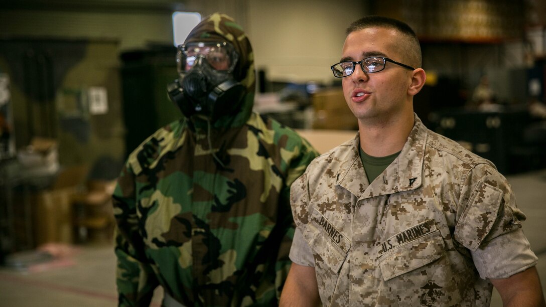 Lance Cpl. Christopher Barnes, chemical, biological, radiological and nuclear defense specialist, Marine Aircraft Group 13, explains the proper use of the joint service, lightweight, integrated suit technology and the M50 joint service general purpose mask during an individual equipment confidence course at building 1980 aboard the Combat Center, Aug. 27, 2015. Following the course, the Marines with Unmanned Aerial Vehicle Squadron 1 and Headquarters Battalion received transport to the confidence chamber at Range 105 for practical application. 