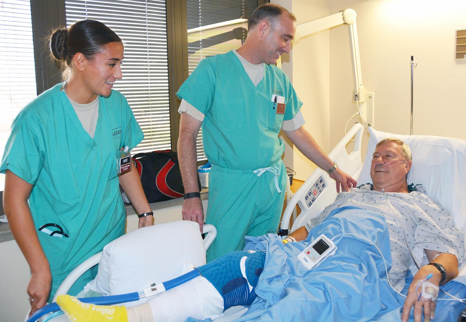 Army Col. Richard Evans (center), deputy commander for nursing, checks on retired Col. Randy Maschek (right) as Pvt. Karinna Ortiz, a practical nurse course student, looks on in the 2 West inpatient ward at the San Antonio Military Medical Center at Fort Sam Houston Aug. 20.