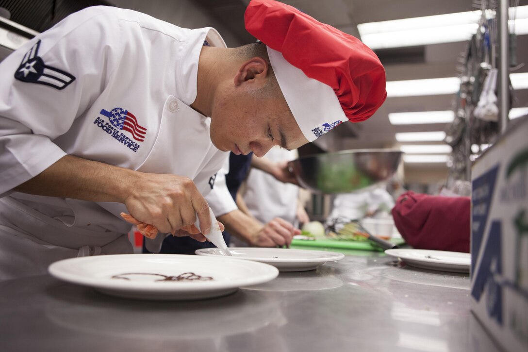 Airman 1st Class Ruel Abastas, a 90th Force Support Squadron chef, decorates a plate with chocolate syrup for a dessert dish during an "Iron Chef" competition at the Chadwell Dining Facility on F.E. Warren Air Force Base, Wyo., Aug. 27, 2015. Chefs from the 90th FSS had to create an entree incorporating the secret ingredient, cheese crackers with peanut butter, along with a dessert dish within the hour time limit. (U.S. Air Force photo/Lan Kim)
