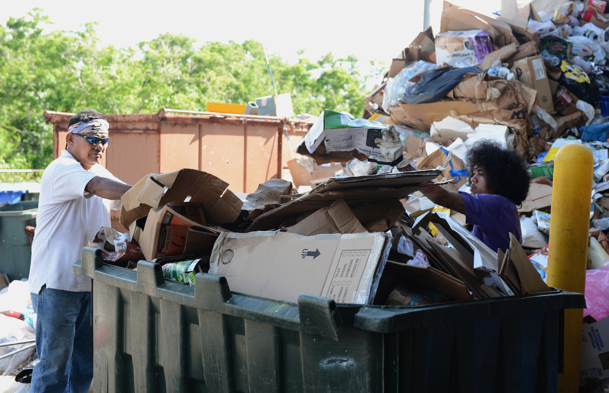 Fernando Culala and Joeven Vencer, temporary refuse collectors at Arc Light Recycling Center, fill a bin with cardboard for it to be used in the multi material baler machine Aug. 28, 2015, at Andersen Air Force Base, Guam. The baler is used to compress recyclable materials such as cardboard and newspapers which produce blocks for easier transportation. (U.S. Air Force photo by Airman 1st Class Arielle Vasquez/Released)