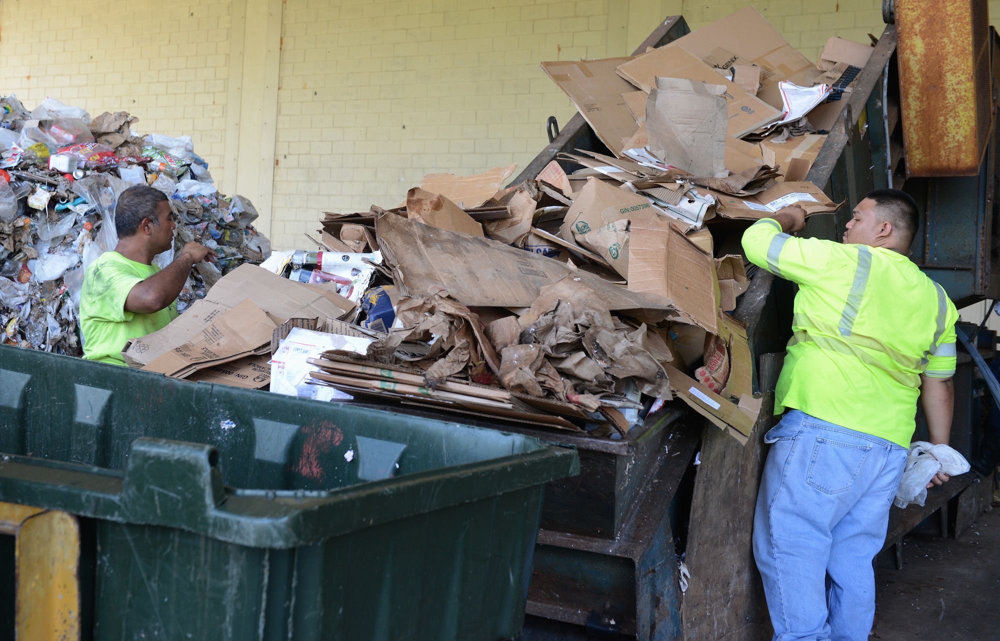 Christopher Ada and Matthew Bidaure, Arc Light Recycling Center refuse collectors, load cardboard on a baler machine’s conveyor belt Aug. 28, 2015, at Andersen Air Force Base, Guam. The baler produces blocks of recyclable materials which are placed in 40- foot containers to be taken to vendors off base for additional processing. (U.S. Air Force photo by Airman 1st Class Arielle Vasquez/Released)