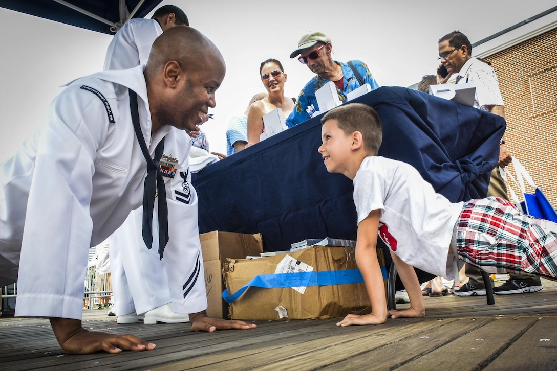 Navy Petty Officer 2nd Class Paul Donaldson executes a pushup with a child during a Navy air show in Atlantic City, N.J., Sept. 2, 2015. Donaldson is a master-at-arms and Navy recruiting scout from Navy Recruiting District Philadelphia. The annual event featured various flight demonstrations and the U.S. Navy Blue Angels. U.S. Navy photo by Petty Officer 1st Class Felicito Rustique
