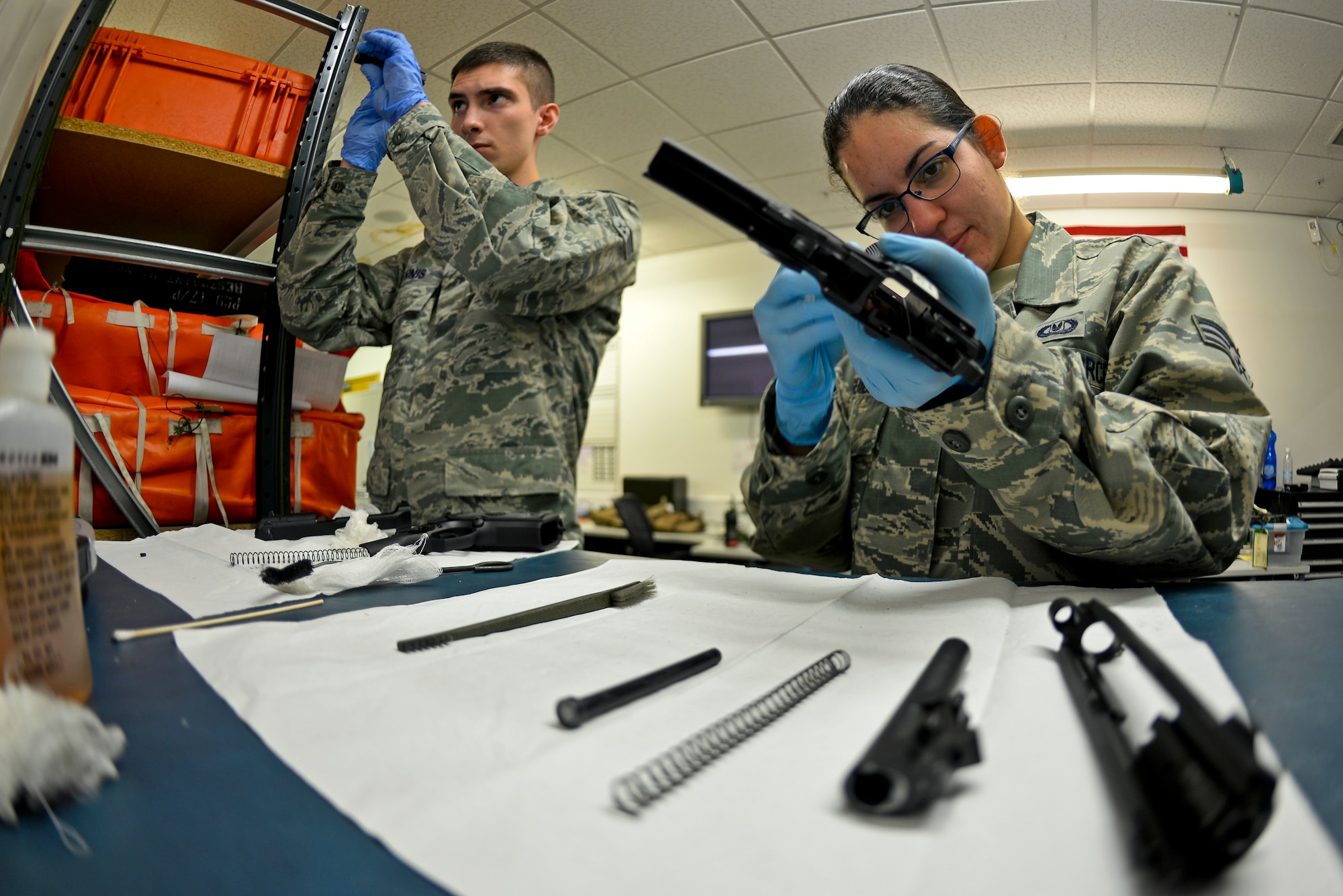 U.S. Air Force Senior Airman Alexandria Delguidice, right, and U.S. Air Force Senior Airman William Ennis, left,  both, 100th Operations Support Squadron Aircraft Flight Equipment journeymen, inspect parts of M-9 pistols Sept. 3, 2015, on RAF Mildenhall, England. Before the firearm can be put together, the barrel assembly, barrel, recoil spring guide, recoil spring and handle must be cleaned and inspected. (U.S. Air Force photo by Staff Sgt. Micaiah Anthony/Released)