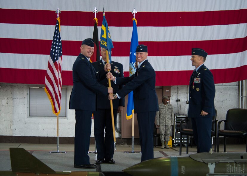 U.S. Air Force Col. Robert Winkler, former 52nd Operations Group commander, right, smiles as U.S. Air Force Col. Joe McFall, 52nd Fighter Wing commander, left, passes the guidon to U.S. Air Force Col. Michael Thompson, 52nd OG command during the 52nd OG change of commander ceremony in Hangar one at Spangdahlem Air Base, Germany, Sep. 4, 2015. The passing on a guidon is tradition in change of command ceremonies. (U.S. Air Force photo by Airman 1st Class Luke Kitterman/Released) 