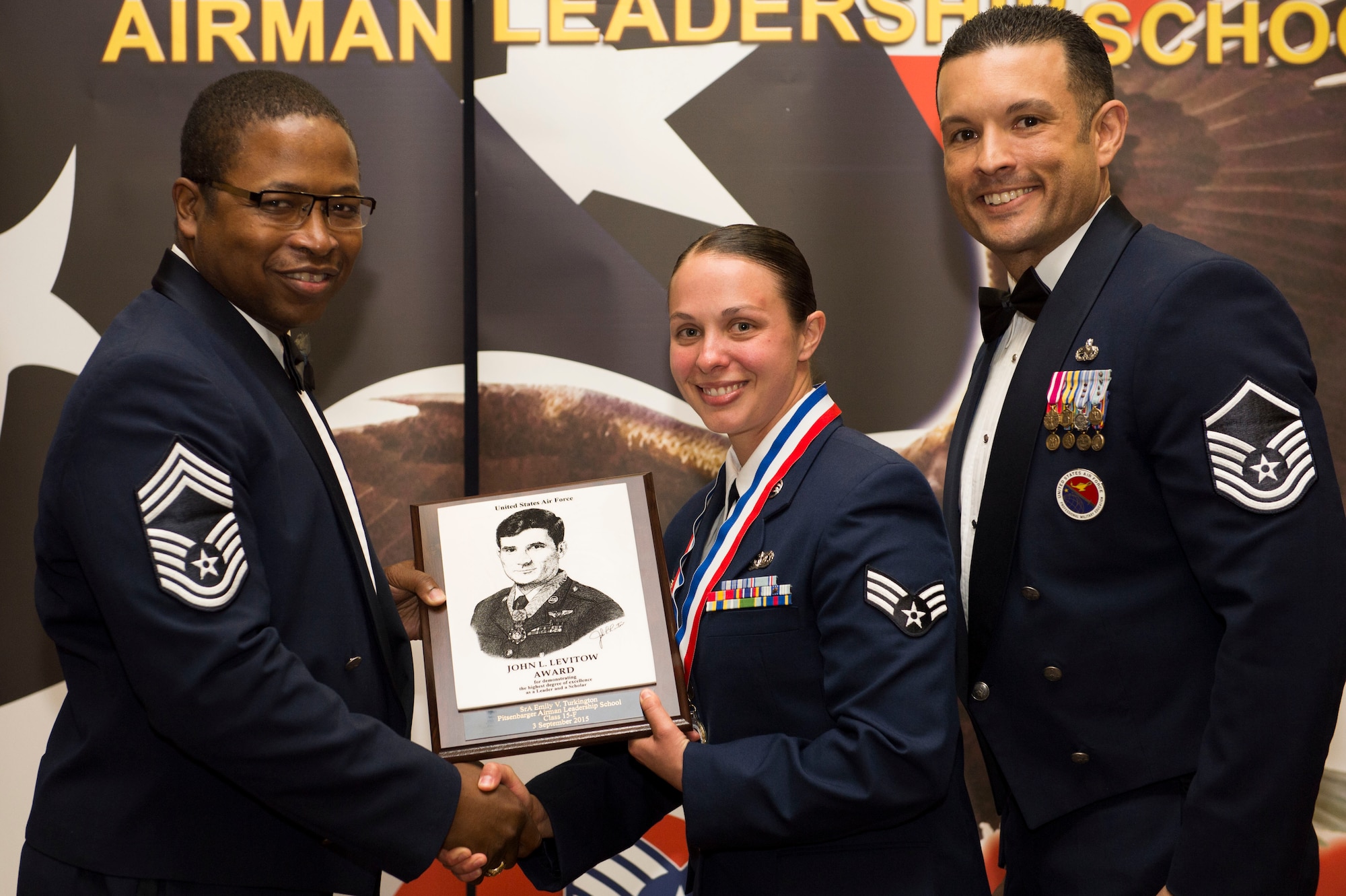 U.S. Air Force Chief Master Sgt. Alvin Holland, a 52nd Medical Group superintendent, left, and U.S. Air Force Master Sgt. Roberto Oregon, Pitsenbarger Airman Leadership School commandant, right, congratulate U.S. Air Force Senior Airman EmilyTurkington, a 52nd Security Forces Squadron patrolman and John L. Levitow Award recipient, center, during the Pitsenbarger ALS Class 15-F graduation ceremony at Club Eifel on Spangdahlem Air Base, Germany, September 3, 2015. The Levitow Award is presented to the student who demonstrated the most outstanding leadership and scholastic qualities based on academic performances and assignment of points by peers and instructors. (U.S. Air Force photo by Airman 1st Class Timothy Kim/Released)