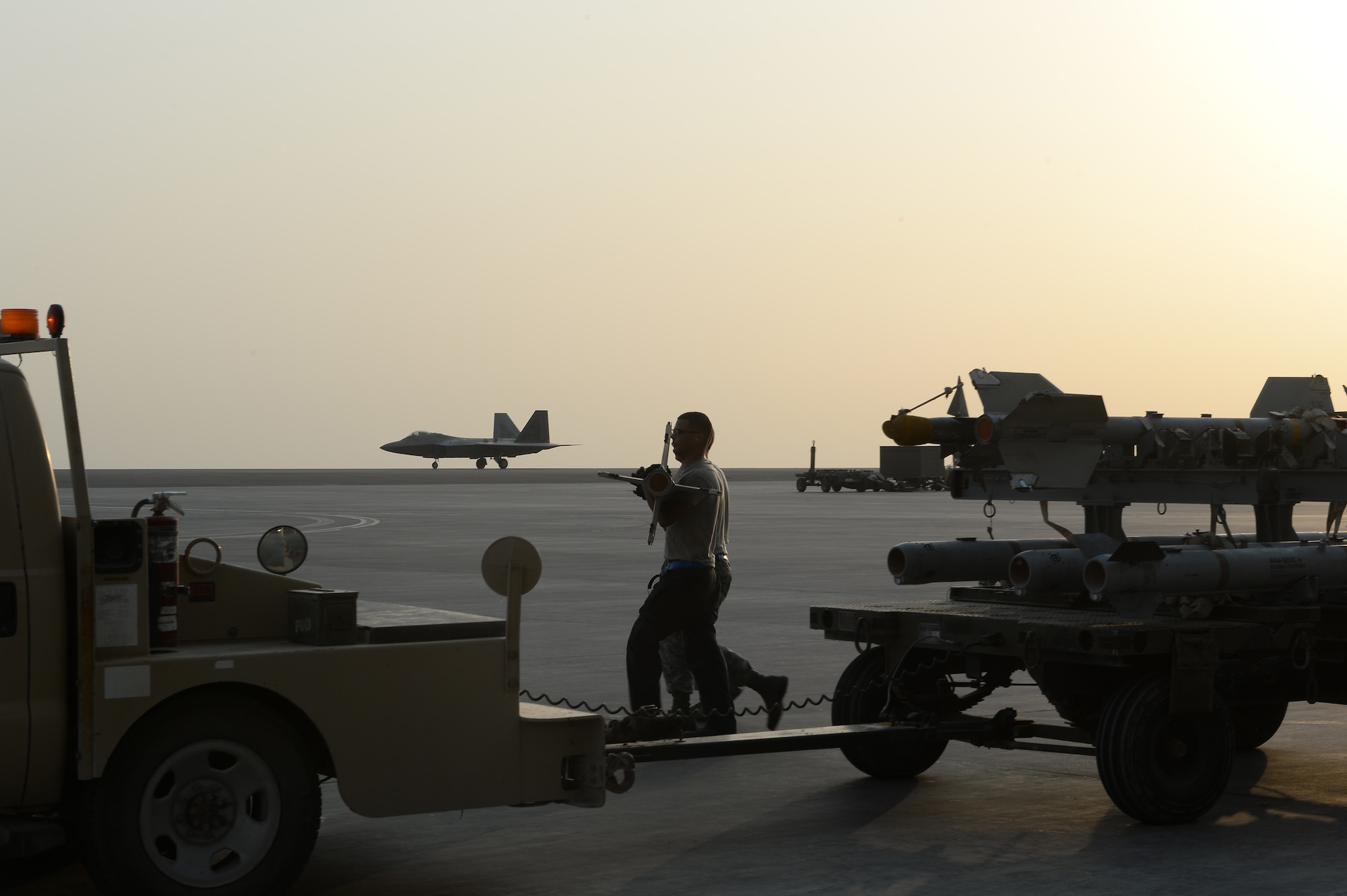 380th Expeditionary Maintenance Airmen prepare to load munitions on an F-22 Raptor while another F-22 Raptor taxis on the runway at an undisclosed location in Southwest Asia, August 30, 2015. The F-22’s combination of sensor capability, integrated avionics, situational awareness, and weapons provides first-kill opportunity against threats. (U.S. Air Force photo/ Staff Sgt. Sandra Welch)
