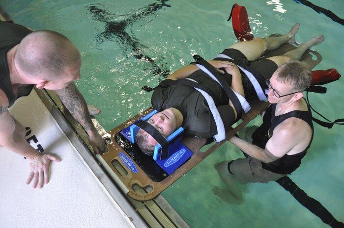 Sgt. David Labell, L, instructor trainer, 2nd Lt. Ward Scott, student at The Basic School, and Sgt. Marshall Breaugh, instructor trainer, conduct annual water survival training with the Fire Station 533 at Ramer Hall Gymnasium, Aug. 4. During the scenario, four Marines dove into a pool and simulated spinal, neck and broken leg injuries. The MCITWS five-man team primarily organizes swim qualifications for lieutenants being trained at The Basic School, to include swim qualifications for the national capital region and the Marine Corps Water Survival Instructor Trainer Course.