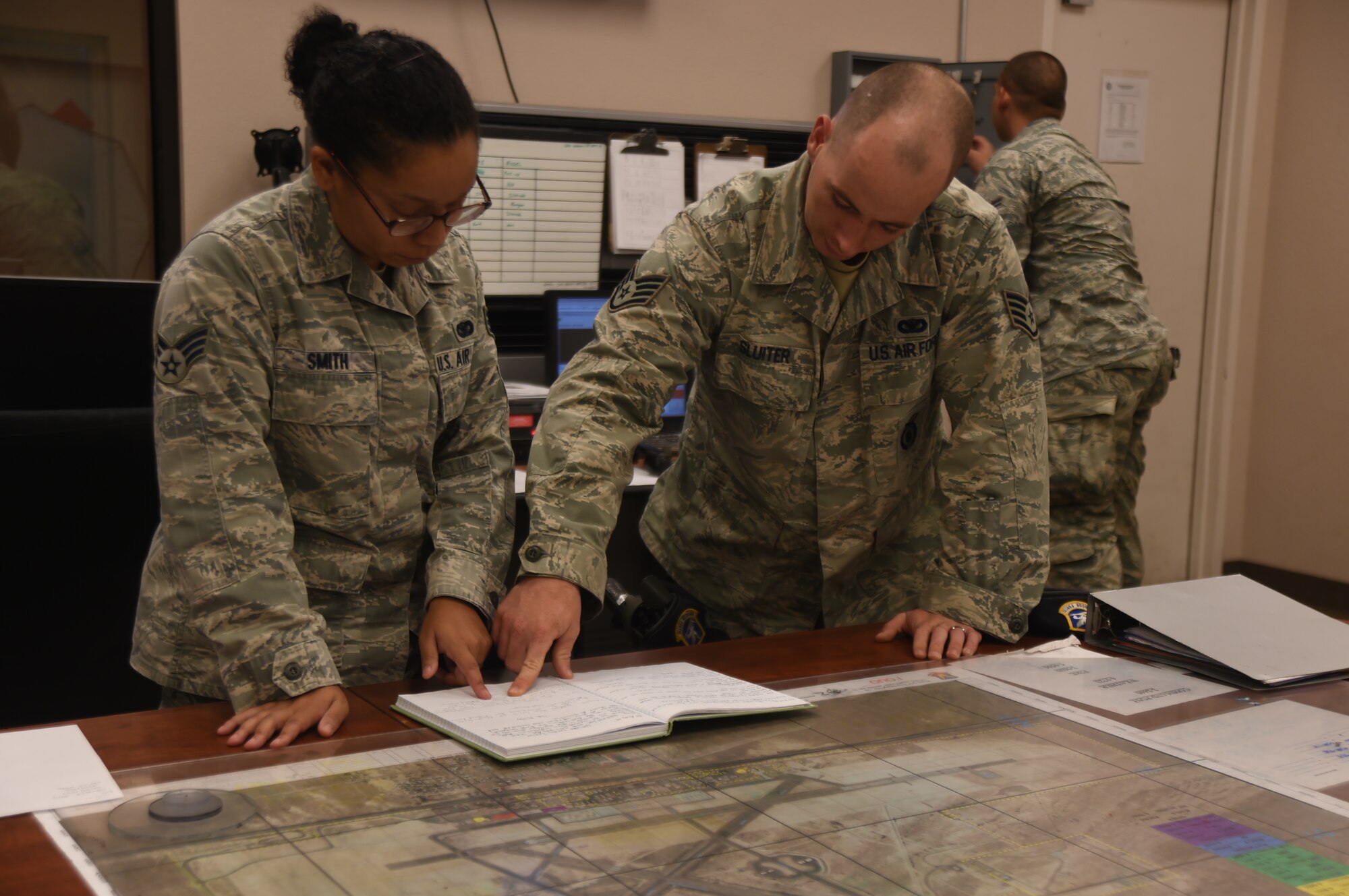Staff Sgt. Kyle Sluiter, 799th SFS BDOC controller provides change-over to Senior Airman Stephanie Smith, 799th SFS Base Defense Operations Center controller, right, during a shift-change at Creech Air Force Base, Nevada, Sept. 2, 2015. The BDOC is the heart of all security forces operations on base and is responsible for securing more than two billion dollars in remotely piloted aircraft, facilities, equipment and personnel. (U.S. Air Force photo by Airman 1st Class Christian Clausen) 