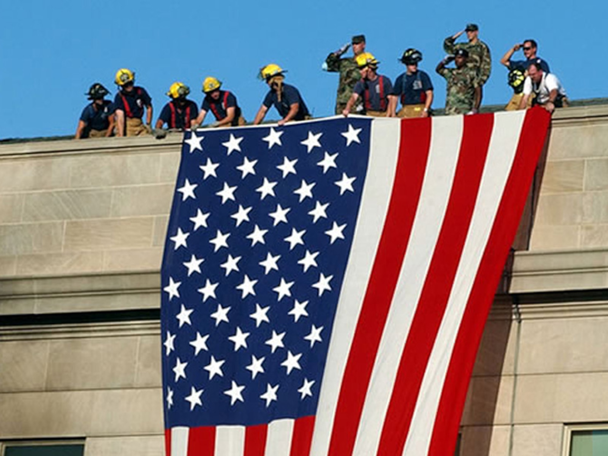 Firefighters and U.S. Army Soldiers unfurl an American flag over the side of the Pentagon during the aftermath of the 9/11 terrorist attack against the building. The Pentagon was the third U.S. building to be struck by al-Qaida militants, Sept. 11, 2001. (Courtesy photo from Reuters/Released)