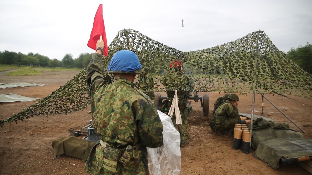 A Japanese Ground Self-Defense Force member holds up a flag showing they are about to fire a  120mm mortar during Forest Light 16-1 at Camp Imazu, Takashima, Japan, Sept. 6, 2015. The JGSDF and U.S. Marines took turns calling fire missions, prepping the mortar for fire, and firing the mortar. Forest Light is a semi-annual, bilateral exercise consisting of a command post exercise and multiple field training events conducted by elements of III Marine Expeditionary Force and the JGSDF.  The JGSDF member is from 50th Infantry Regiment, 14th Brigade.