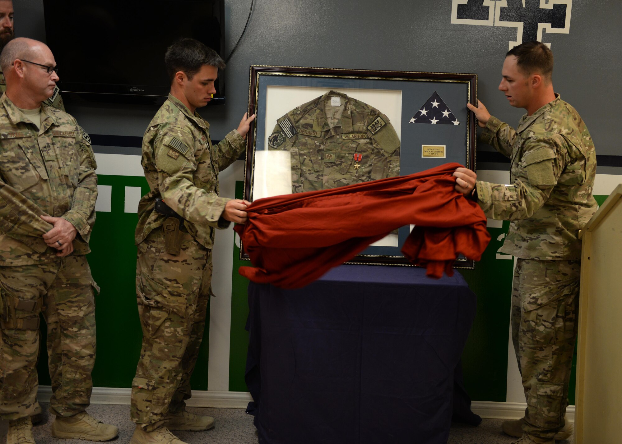 U.S Air Force Senior Airman  James McKinney, left, and Staff Sgt. Kyle Henderson, Task Force Crimson expeditionary detachment 2405 team members, remove a sheet from a shadowbox dedicated to fallen hero Staff Sgt. Todd Lobraico during a dedication remembrance  ceremony Sept. 5, 2015, at Bagram Airfield, Afghanistan. Members of BAF gathered to remember the sacrifice made by Lobraico when he lost his life during a fire fight against enemy forces while deployed here in 2013. (U.S. Air Force photo by Senior Airman Cierra Presentado/Released)  