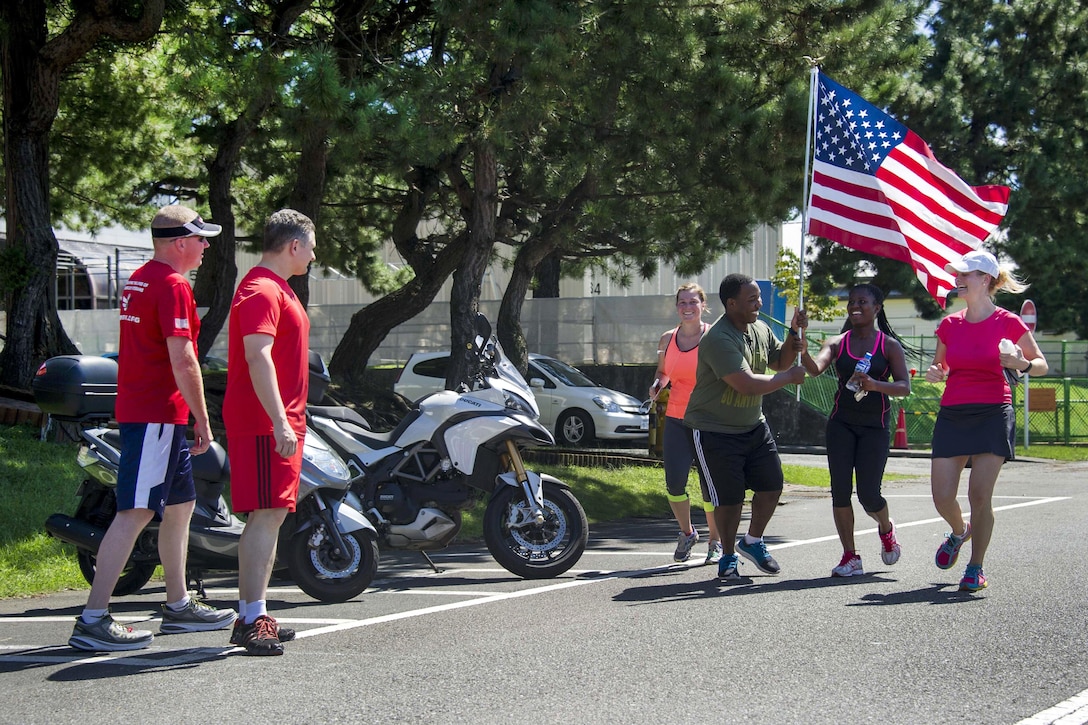 U.S. Navy Petty Officer 2nd Class Zacchaeus Glass takes the American flag from Team Red, White and Blue members during a 9/11 memorial run on Naval Air Facility Atsugi, Japan, Sept. 11, 2015. U.S. Navy photo by Petty Officer 3rd Class Ryan G. Greene