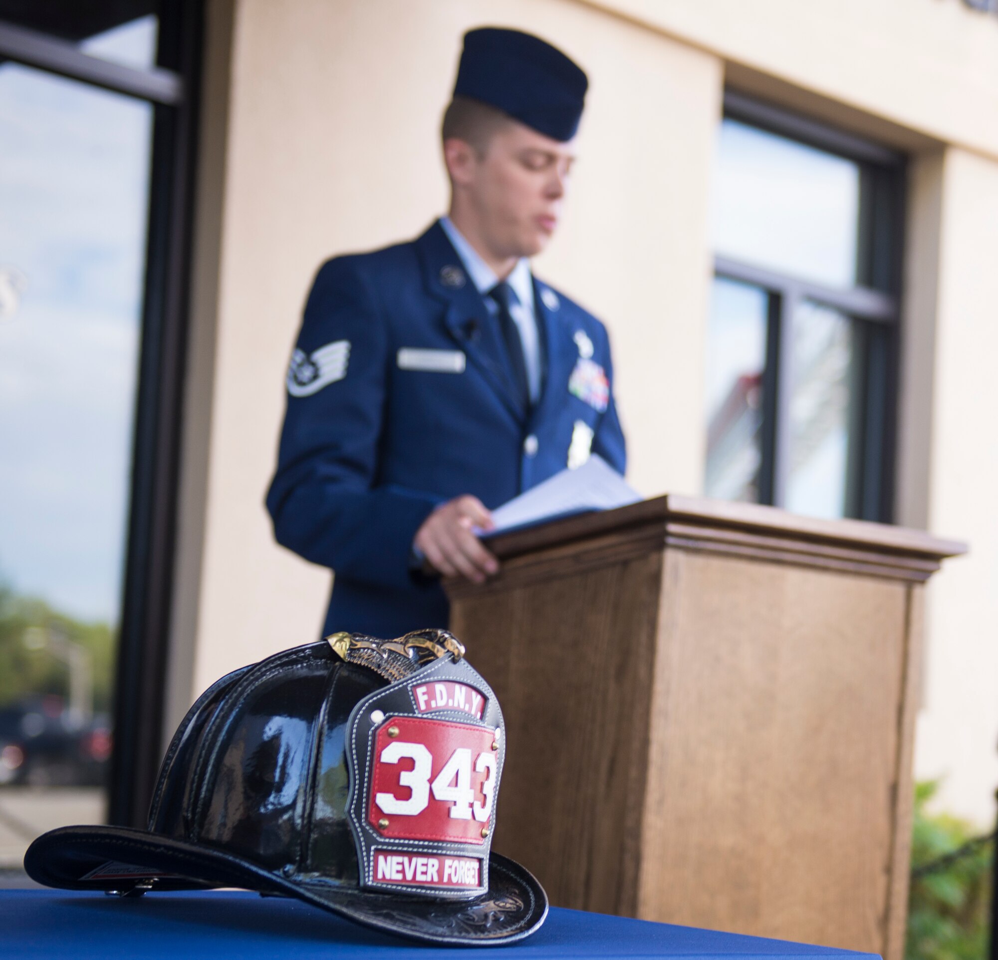 A firefighter helmet rests in honor of fallen 9/11 first responders as U.S. Air Force Staff Sgt. Christopher Conroy, 23d Civil Engineer Squadron fire protection crew chief, provides opening remarks during a 9/11 remembrance ceremony Sept. 11, 2015, at Moody Air Force Base, Ga. Among those who perished during the 9/11 attacks were 343 firefighters and paramedics and 23 law enforcement officers. (U.S. Air Force photo by Airman 1st Class Greg Nash/Released)