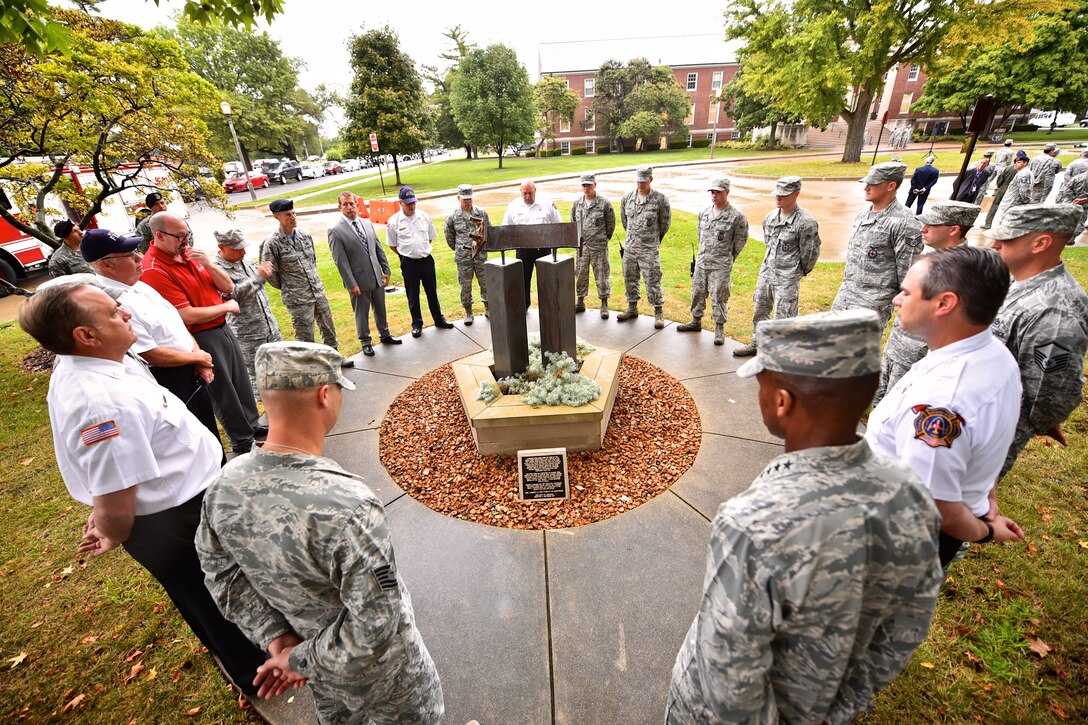 Just before the 7:40am Patriot Day ceremony members of Team Scott join together around the 9/11 Memorial for a moment of silence and reflection, Sept. 11, 2015, Scott Air Force Base, Illinois.  The memorial consists of a planter that is shaped like the Pentagon and is constructed of Indiana limestone--the same material used in the building's facade. Within the planter, foliage representing life is planted in soil from Shanksville, Pennsylvania. Emerging from the center are the Twin Tower replicas, made of the same type of brushed steel used on the towers. Capping off the memorial is a portion of a steel beam from the World Trade Center. (U.S. Air Force photo by Christopher Parr)