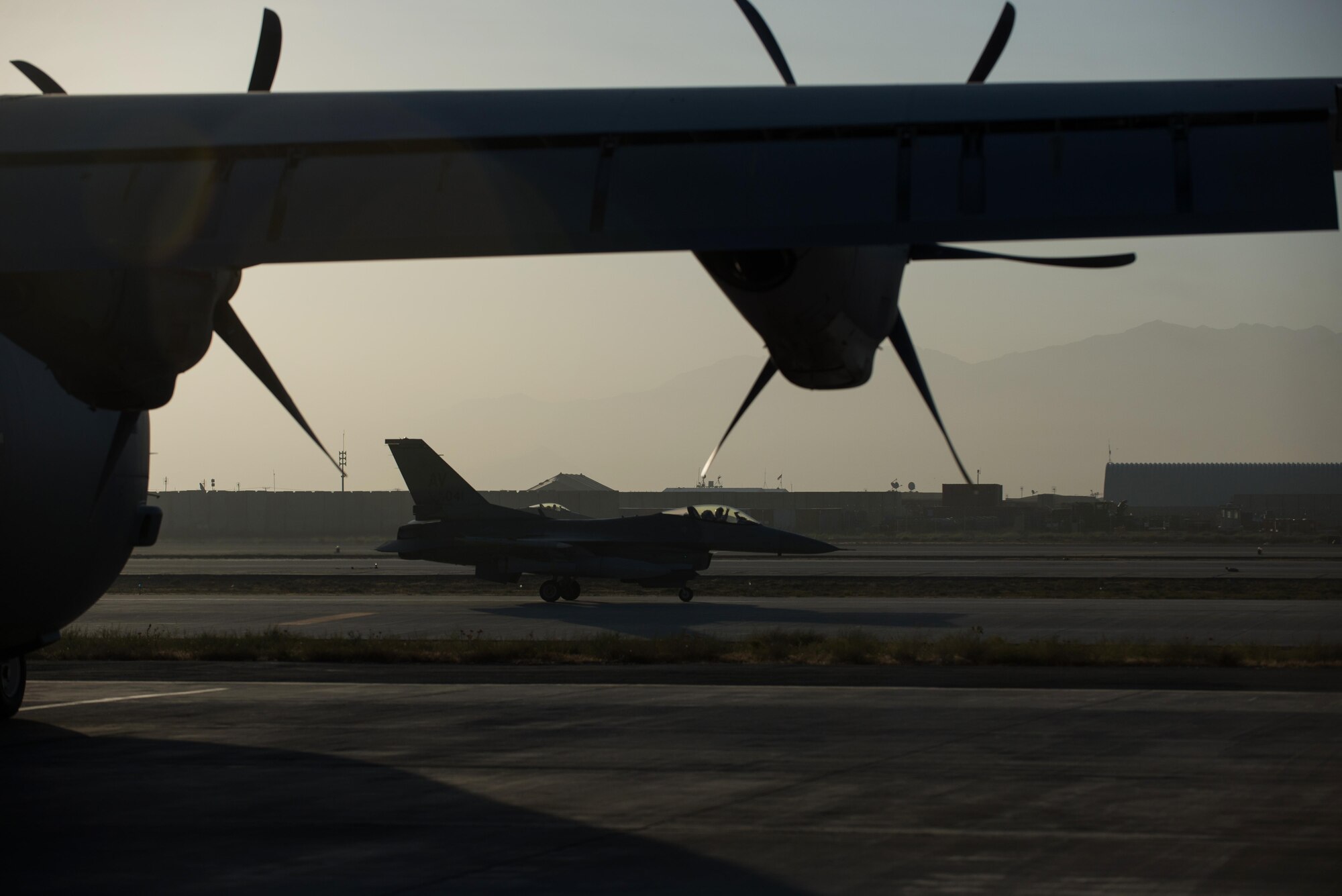 A U.S. Air Force F-16 Fighting Falcon pilot wave’s goodbye as he passes C-130J Super Hercules aircraft and Airmen assigned to the 774th Expeditionary Airlift Squadron as they prepare to depart Bagram Airfield, Afghanistan, Sept. 12, 2015. The squadron was in the process of redeploying back to Little Rock Air Force Base after successfully completing their deployment. During their rotation as the 774th Expeditionary Airlift Squadron, the Little Rock team completed 1,850 combat sorties and moved 14,500 passengers and 17 million pounds of cargo.  (U.S. Air Force photo by Tech. Sgt. Joseph Swafford/Released)
