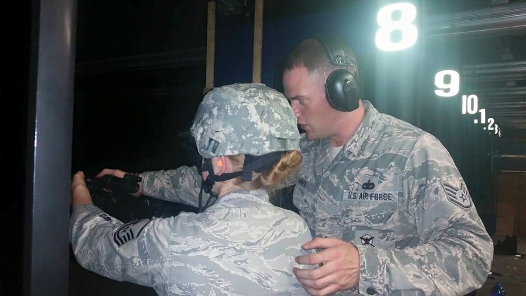 Staff Sgt. Brian Davies assists Master Sgt. Susan Flannery as she shoots using night vision goggles and a targeting laser at the Enfield Department of Corrections indoor firing range Aug. 1, 2015.  (U.S. Air National Guard photos by Tech. Sgt. Jessica Roy)