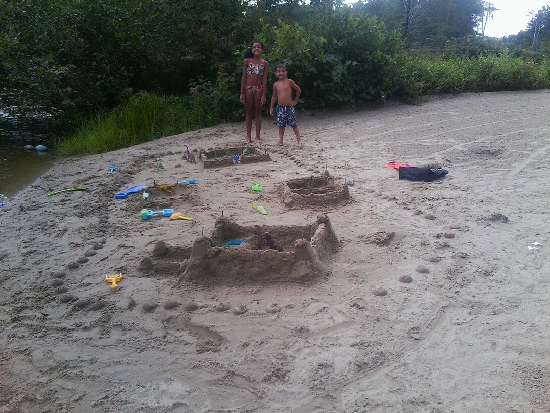 Two young sand castle contestants stand proudly next to their creations.