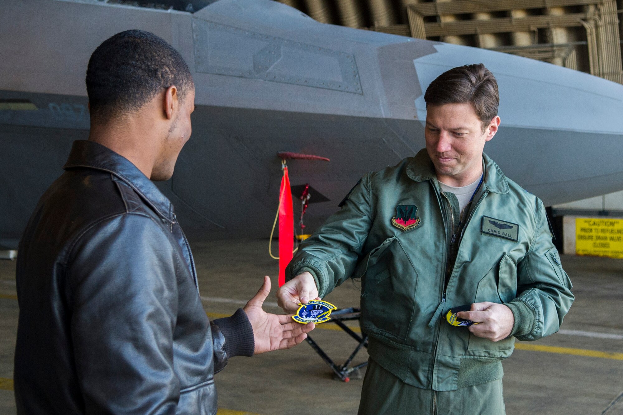 U.S. Air Force Capt. Chris Ball, 95th Fighter Squadron F-22 Raptor fighter aircraft pilot, gives a 95th FS patch to a Bitburg Middle-High School student during a tour of an F-22 in a hardened aircraft shelter at Spangdahlem Air Base, Germany, Sept. 10, 2015. In addition to the tour, the F-22 pilots interacted with students at Spangdahlem Middle School the day prior. (U.S. Air Force photo by Airman 1st Class Luke Kitterman/Released)
