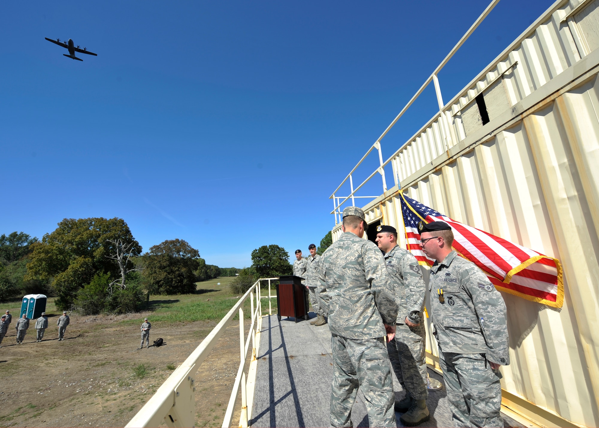A C-130J flies overhead while Col. Charles Brown, 19th Airlift Wing commander, presents two 19th Security Forces Squadron Defenders the Air Force Commendation Medal for their acts of courage Sept. 14, 2015, at Military Operations Urban Terrain (MOUT) Village on Little Rock Air Force Base, Ark. The two members engaged and neutralized a threat June 15, 2015, protecting base personnel and government assets. (U.S. Air Force photo by Senior Airman Scott Poe)