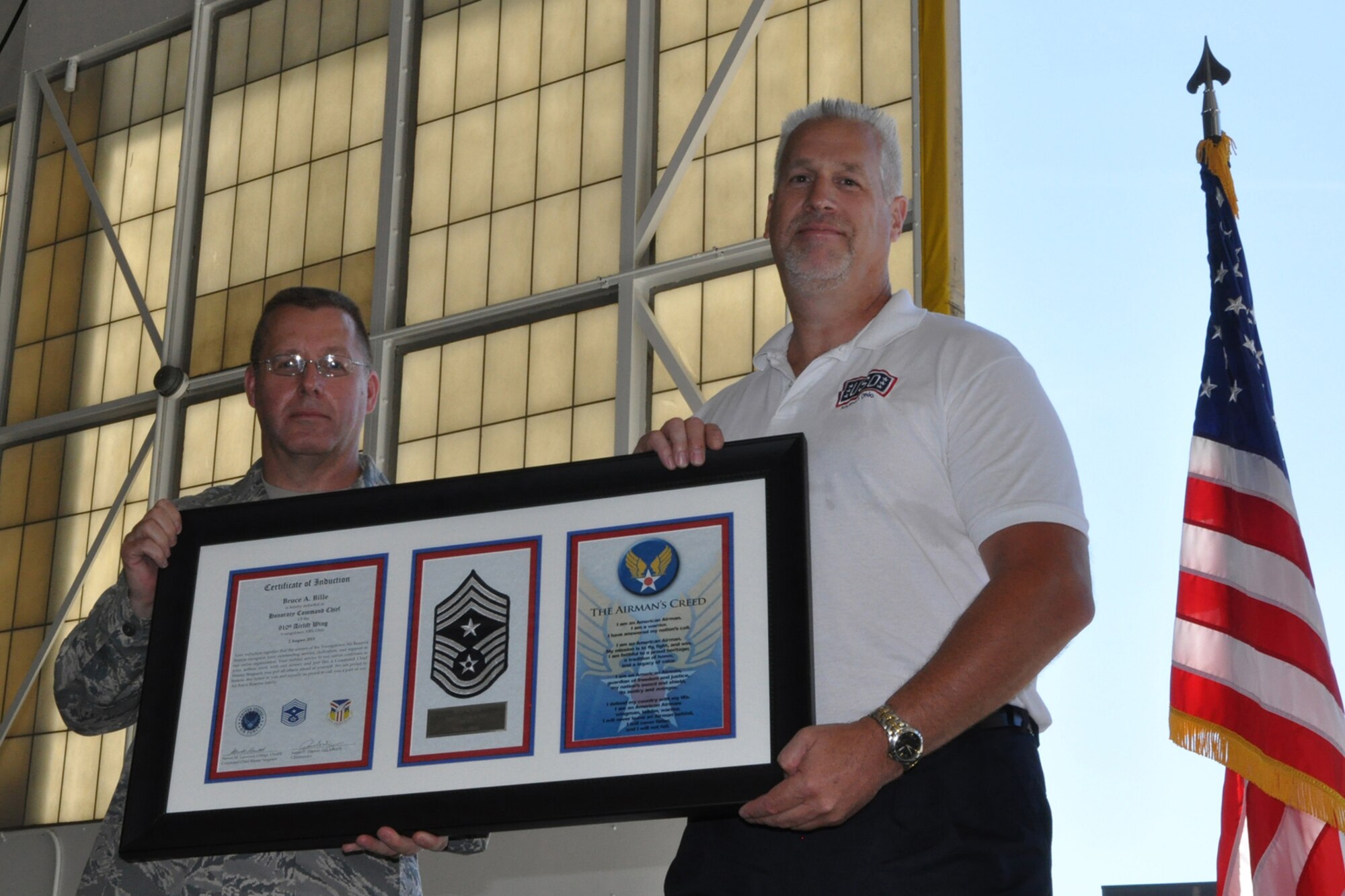 Chief Master Sgt. Steven Larwood, 910th Airlift Wing Command Chief, and Mr. Bruce Bille, director of the USO Lounge at YARS, hold a framed memento honoring Bille as the 910th’s first Honorary Command Chief during the Family Day Commander’s Call held here, Aug. 2, 2015. Family day is an installation open house held for 910th Servicemembers and their families, designed to let Reserve families strengthen bonds and experience the home station of their Reservist loved one. (U.S. Air Force photo/Master Sgt. Bob Barko Jr.)