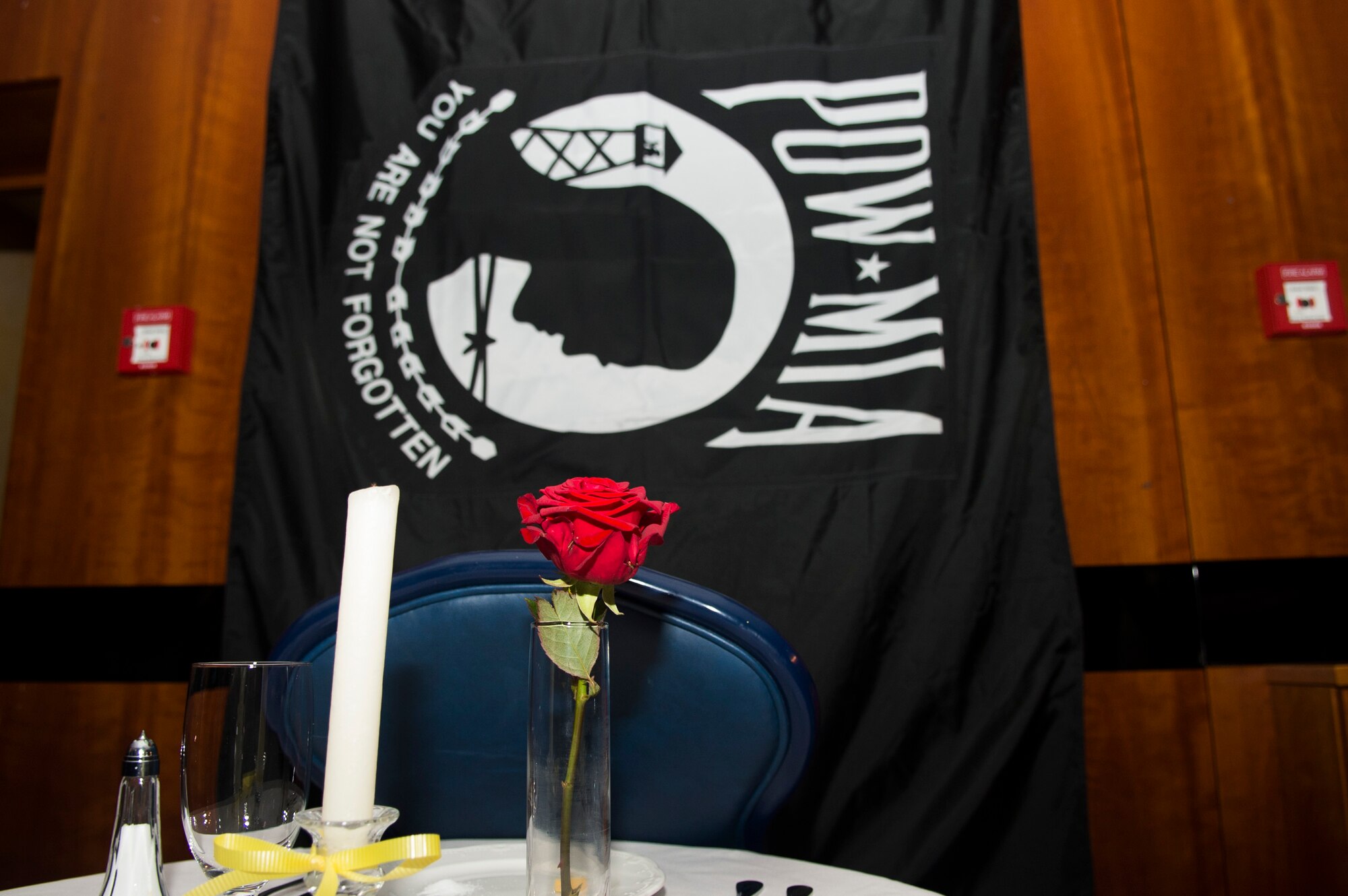 A set table sits in front of a prisoner-of-war/missing-in-action flag during the Spangdahlem Air Force Ball in Club Eifel on Spangdahlem Air Base, Germany, Sept. 12, 2015. An Airman set the table and lit a candle in honor of the POW/MIA. (U.S. Air Force photo by Airman 1st Class Luke Kitterman/Released)   